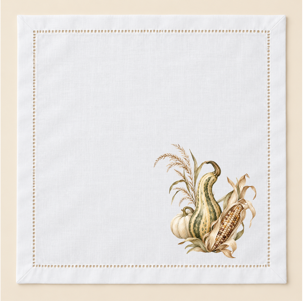 White 20-inch hemstitched cotton napkin with a hand-pressed fall botanical design featuring wheat, gourds, and muted olive and cream tones.