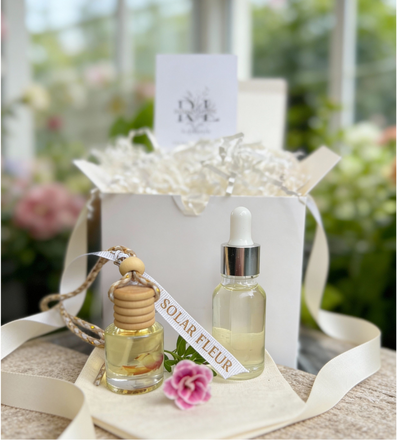 Car Coastal car diffuser gift set with refill bottle and muslin bag styled in front of white box with raffia paper, ribbon accents, and soft blurred greenery backdrop