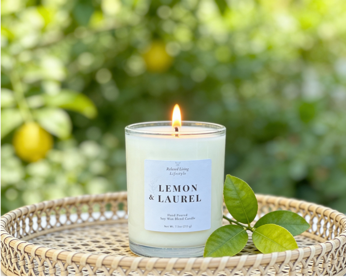 Lemon & Laurel candle 7.5 oz burning in woven basket with greenery accent, set against a soft greenery backdrop in natural light