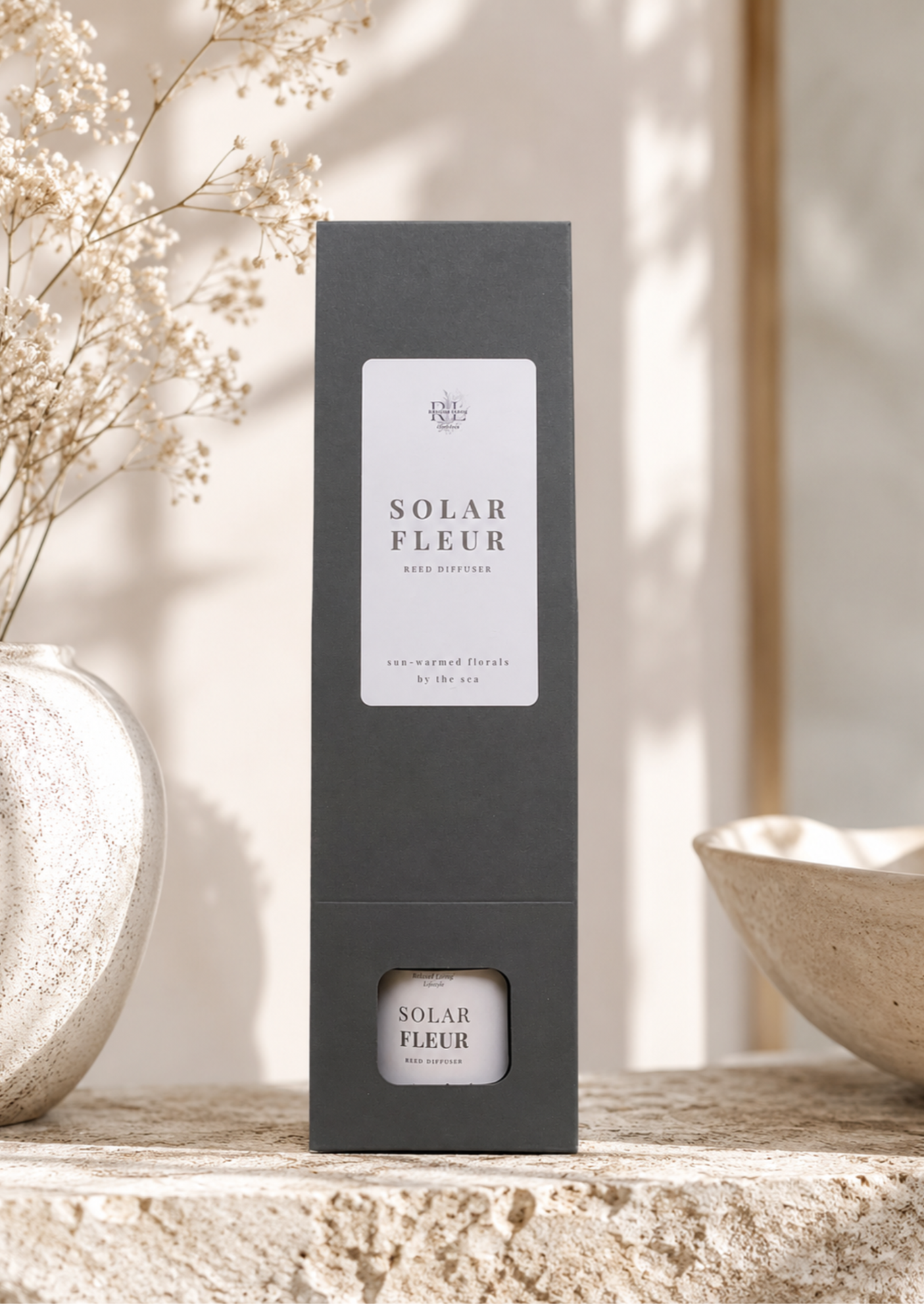 Solar Fleur reed diffuser gift box displayed on a textured stone surface with soft natural light, decorative ceramic accents, and delicate dried florals