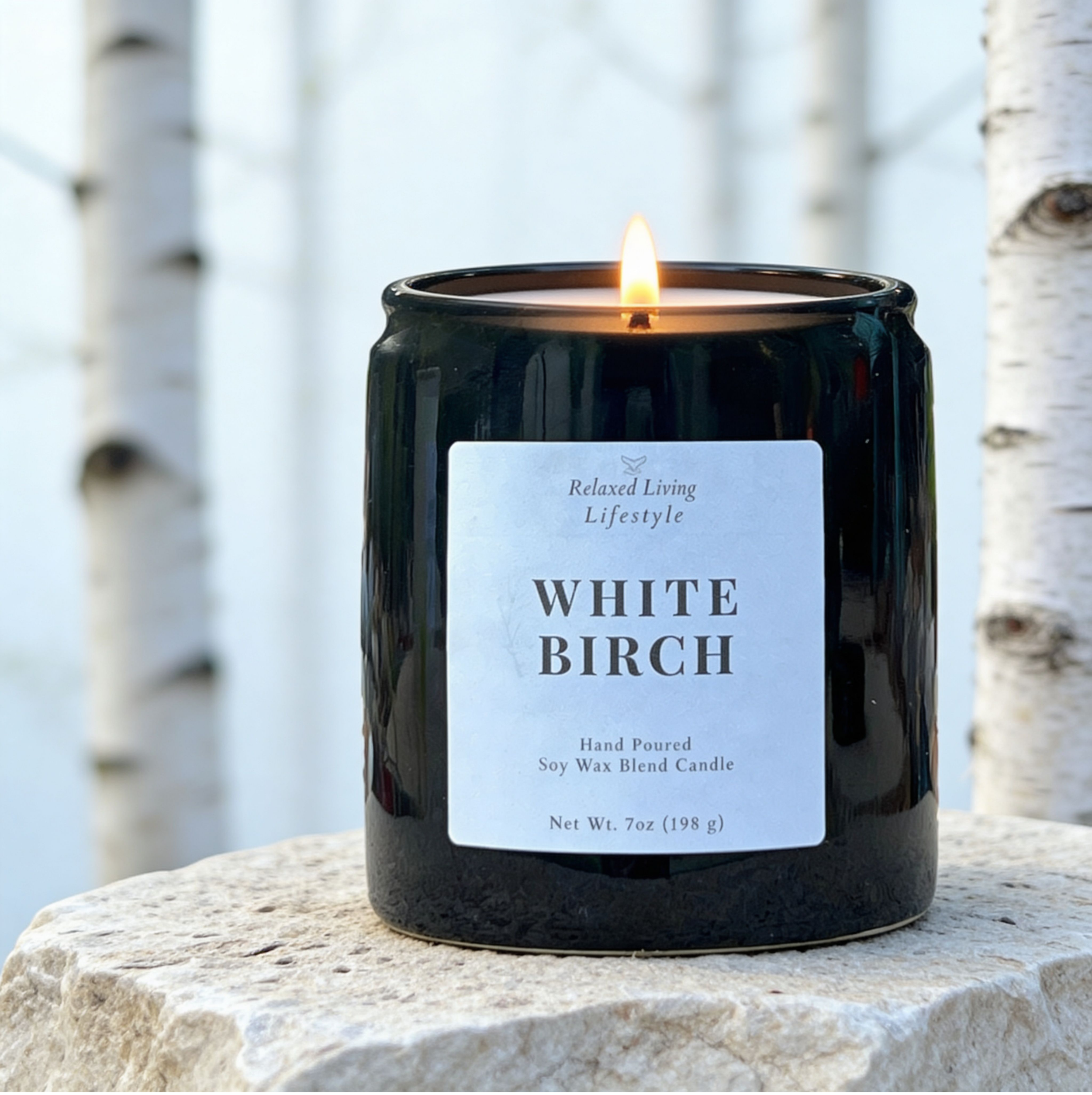 White Birch soy candle lit 7 oz on textured surface with blurred birch tree background in soft natural light