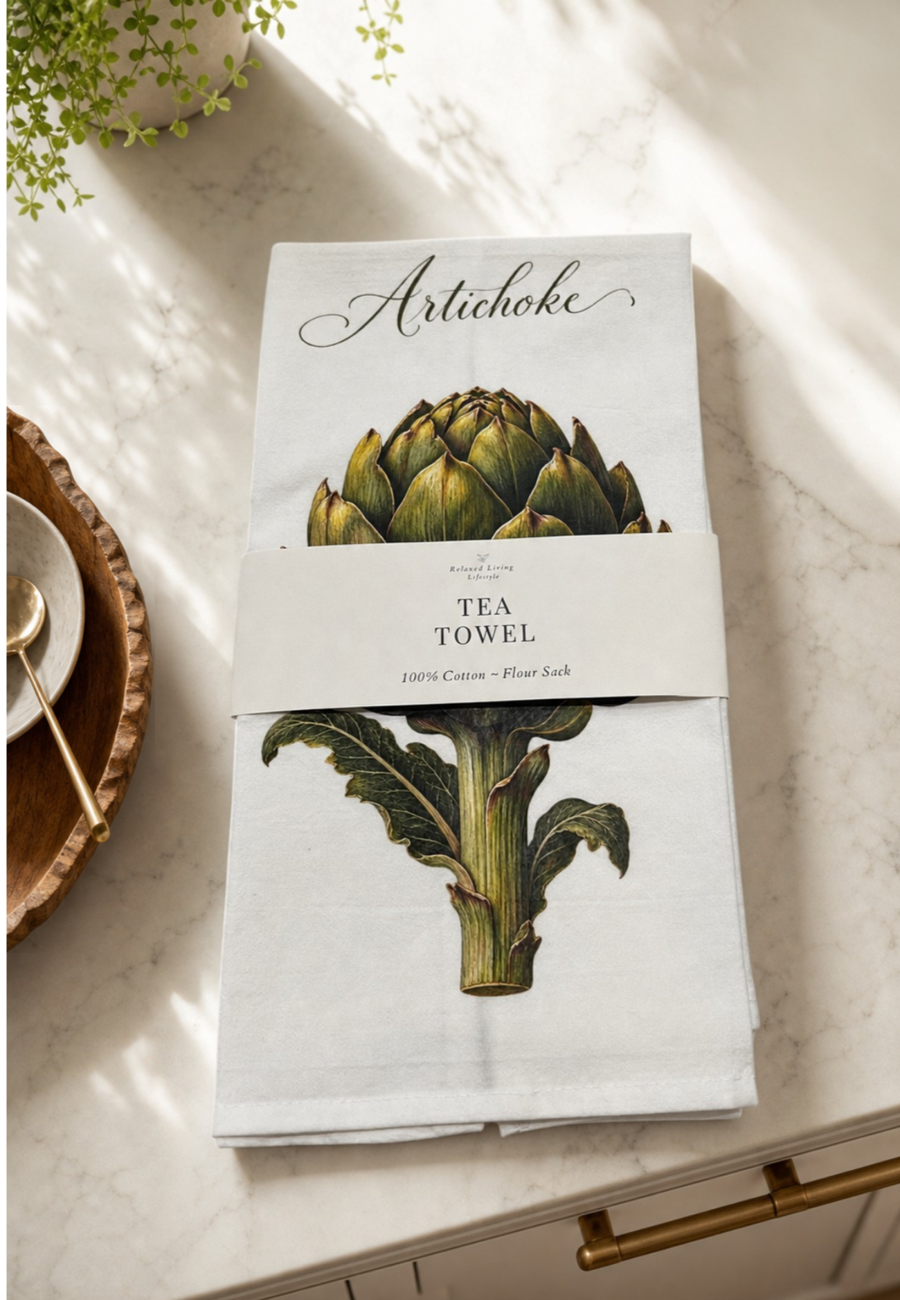 Botanical artichoke print cotton tea towel, banded label, styled on marble counter in a bright luxury kitchen
