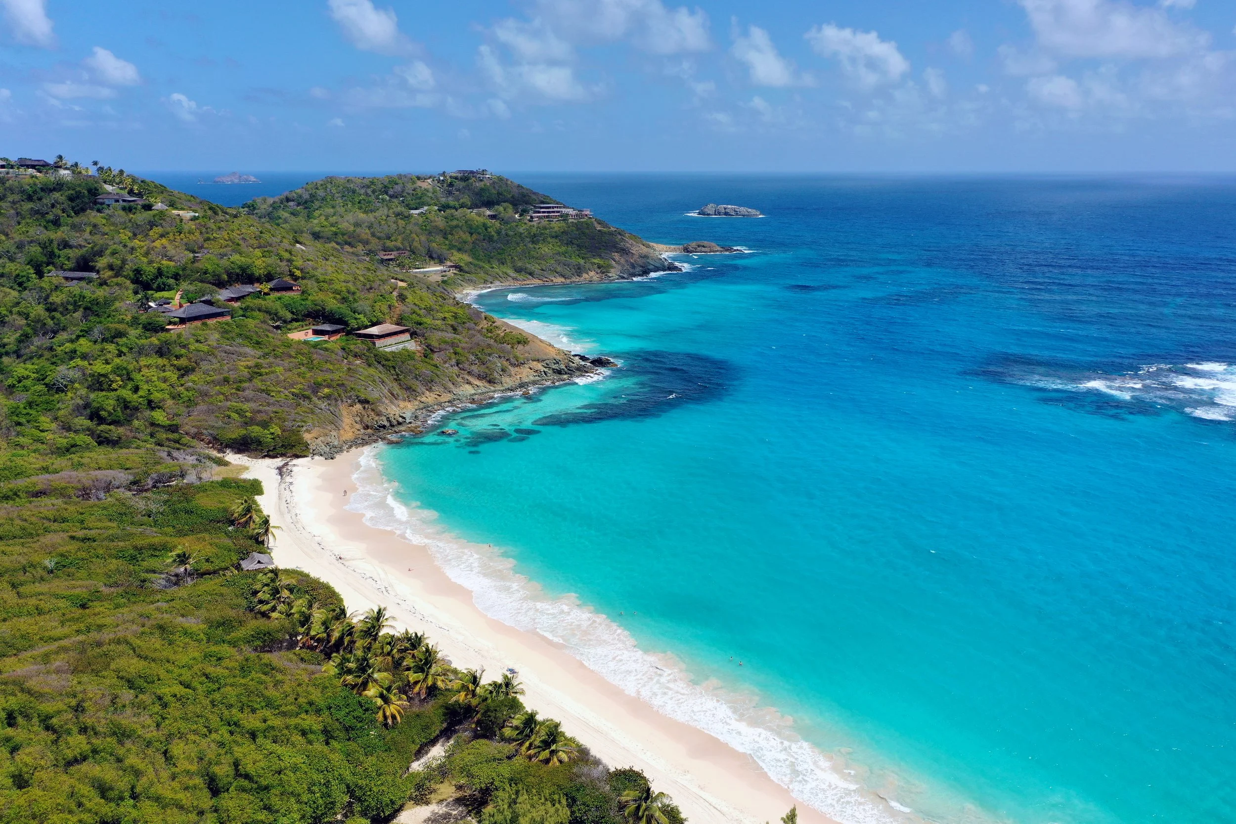 Aerial view of a tropical beach with turquoise water and lush greenery on cliffs.