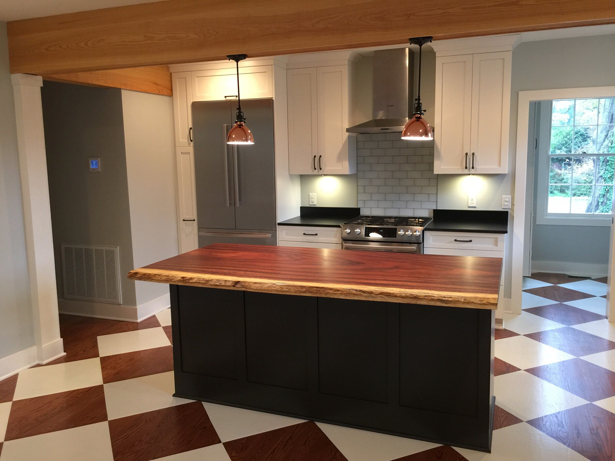 Modern kitchen with white cabinets, stainless steel appliances, wooden island countertop, pendant lighting, and a checkered floor.