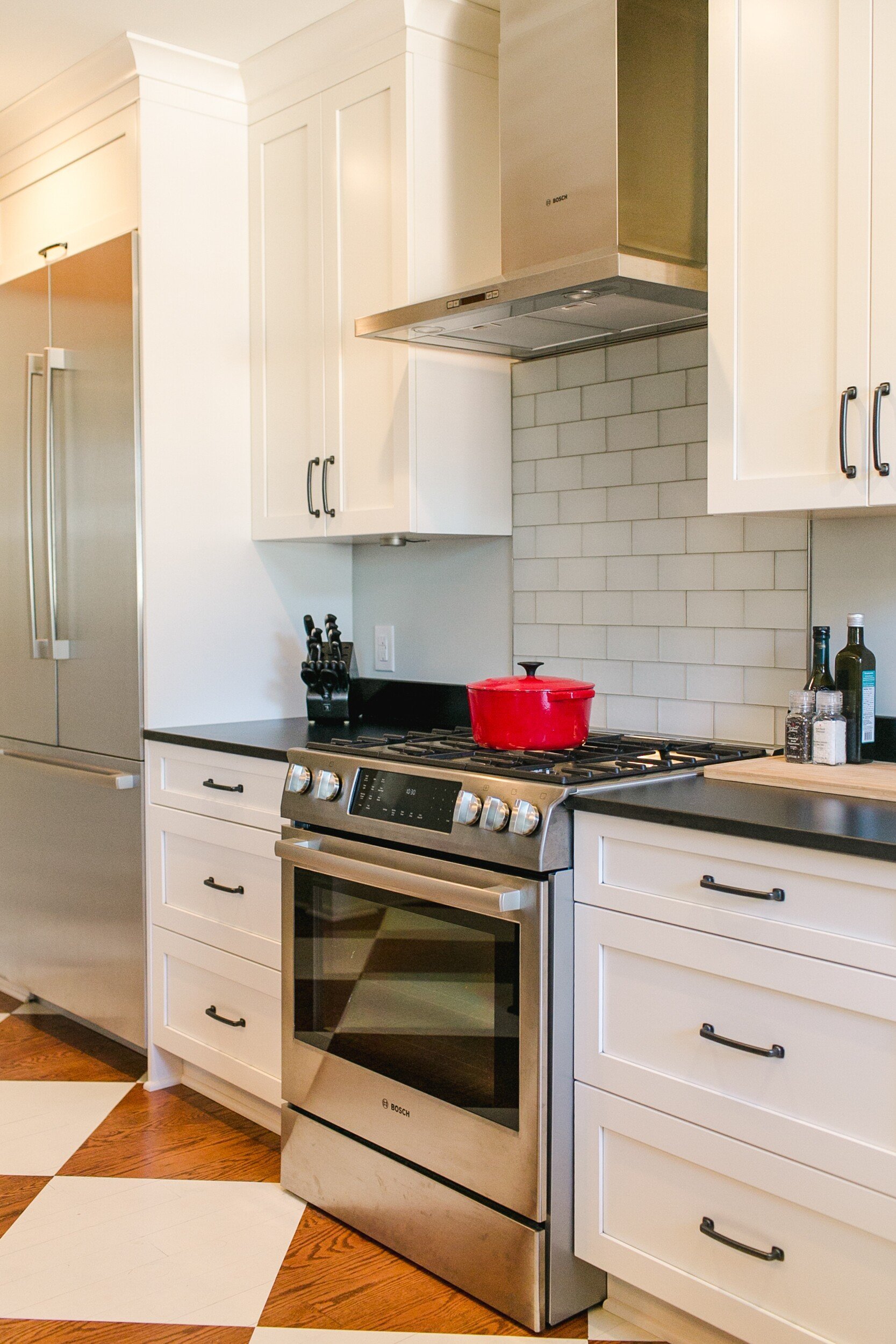 Modern kitchen with stainless steel appliances, white cabinets, subway tile backsplash, and a red pot on the stove.
