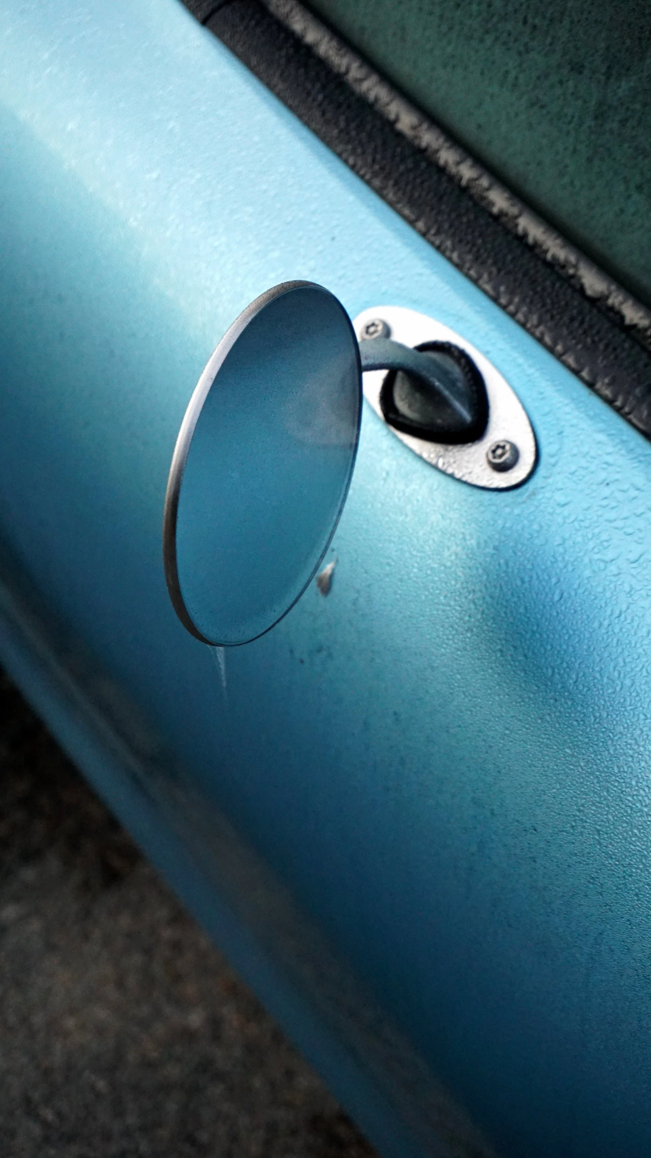 Close-up of a round side mirror on a light blue vehicle.