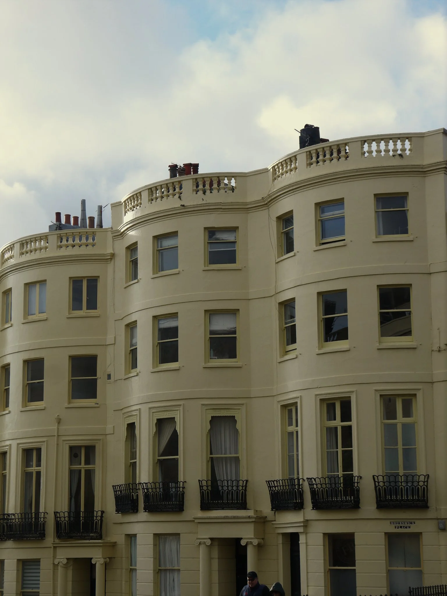 Victorian-style four-story building with cream facade, multiple windows, and small balconies, under a cloudy sky.