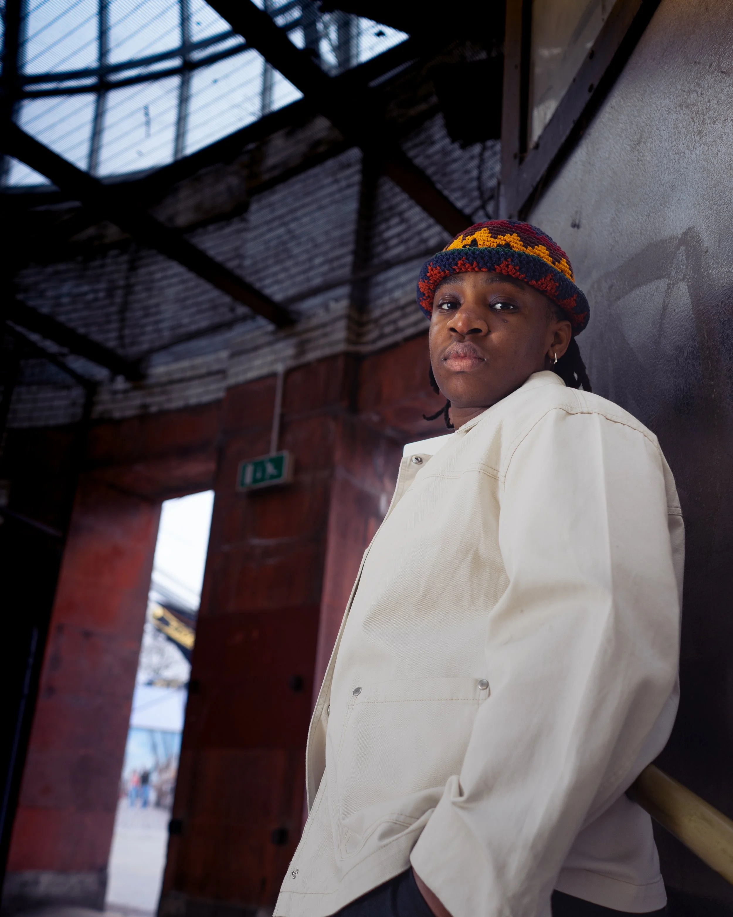 Person wearing a colorful knit hat and white jacket standing in a dim industrial setting.