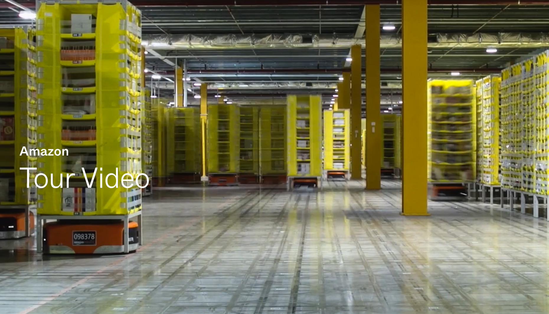 Interior of an Amazon warehouse with yellow shelves and autonomous delivery robots moving along the floor.