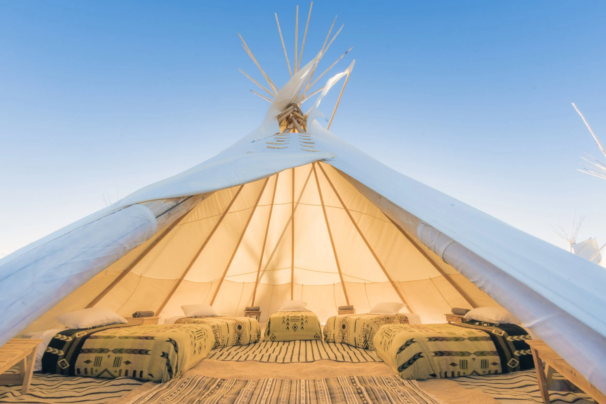 Inside a large tent with cushions and pillows, the tent is illuminated from inside with a soft glow, and the sky is clear and blue outside.
