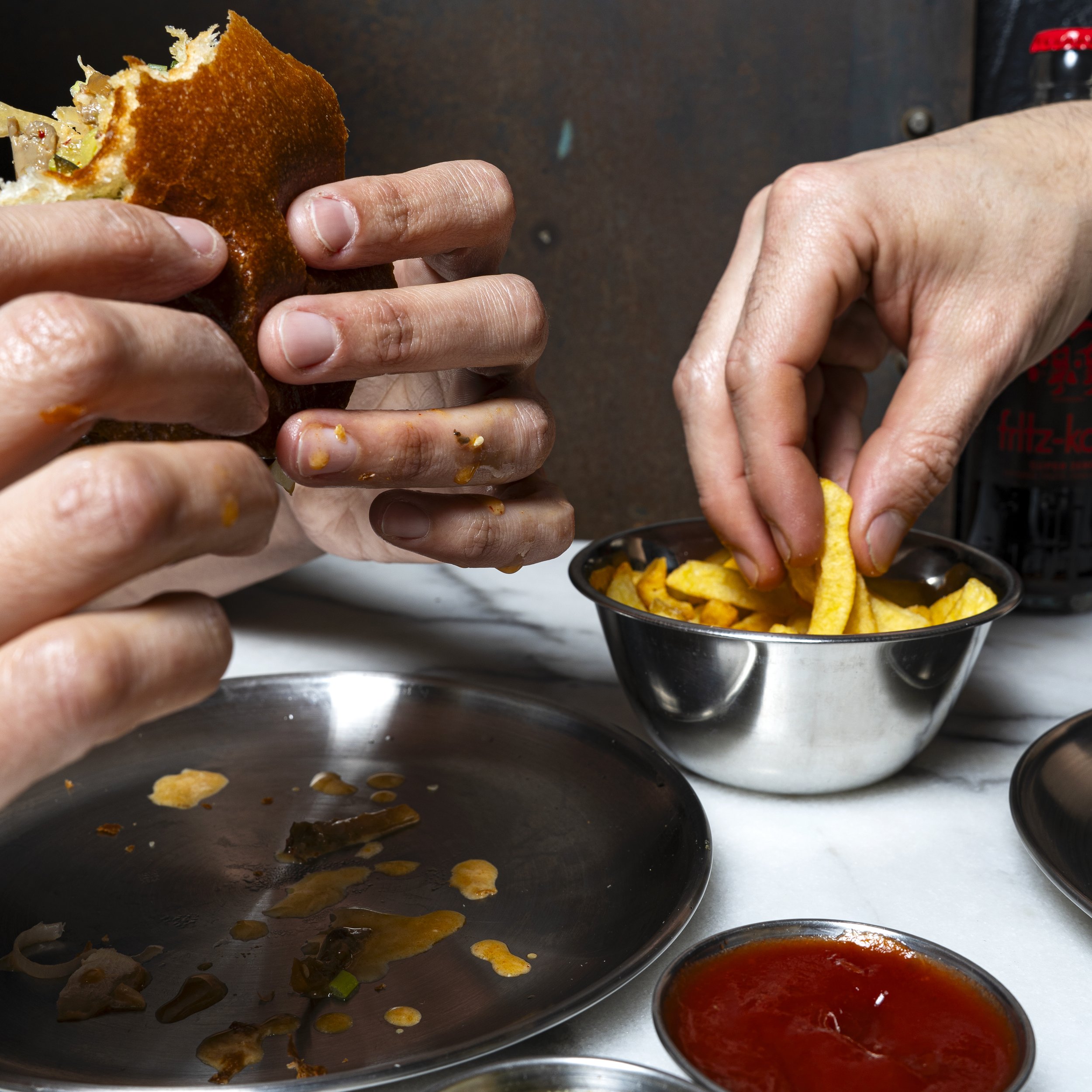 Close-up of hands preparing a vegan burger, served with crispy fries and plant-based sauces.
