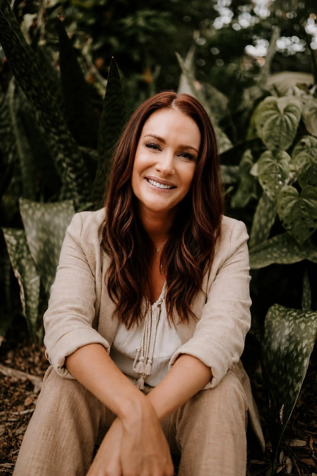Katie Robinson, IFS therapist, sitting in a lush, green outdoor setting wearing a linen blazer