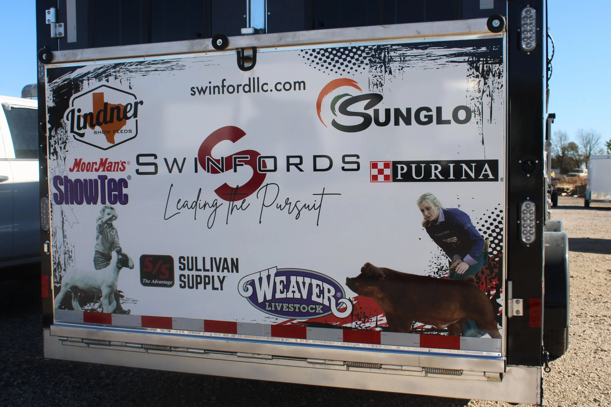 A large promotional trailer displaying logos of various agricultural and livestock brands, including Lindner, Swifords, Purina, SunGlo, MoorMans, ShowTec, Sullivan Supply, and Weaver Livestock. The trailer also features a photo of a woman with blonde