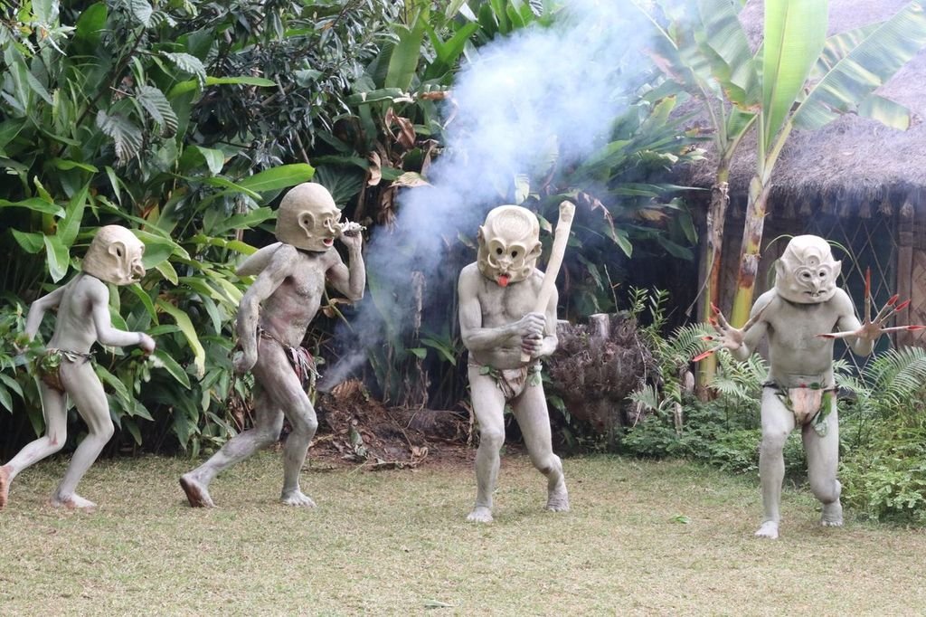 Asaro Mudmen performing in traditional clay masks and body paint during a cultural ceremony in Papua New Guinea, surrounded by lush tropical vegetation and village huts
