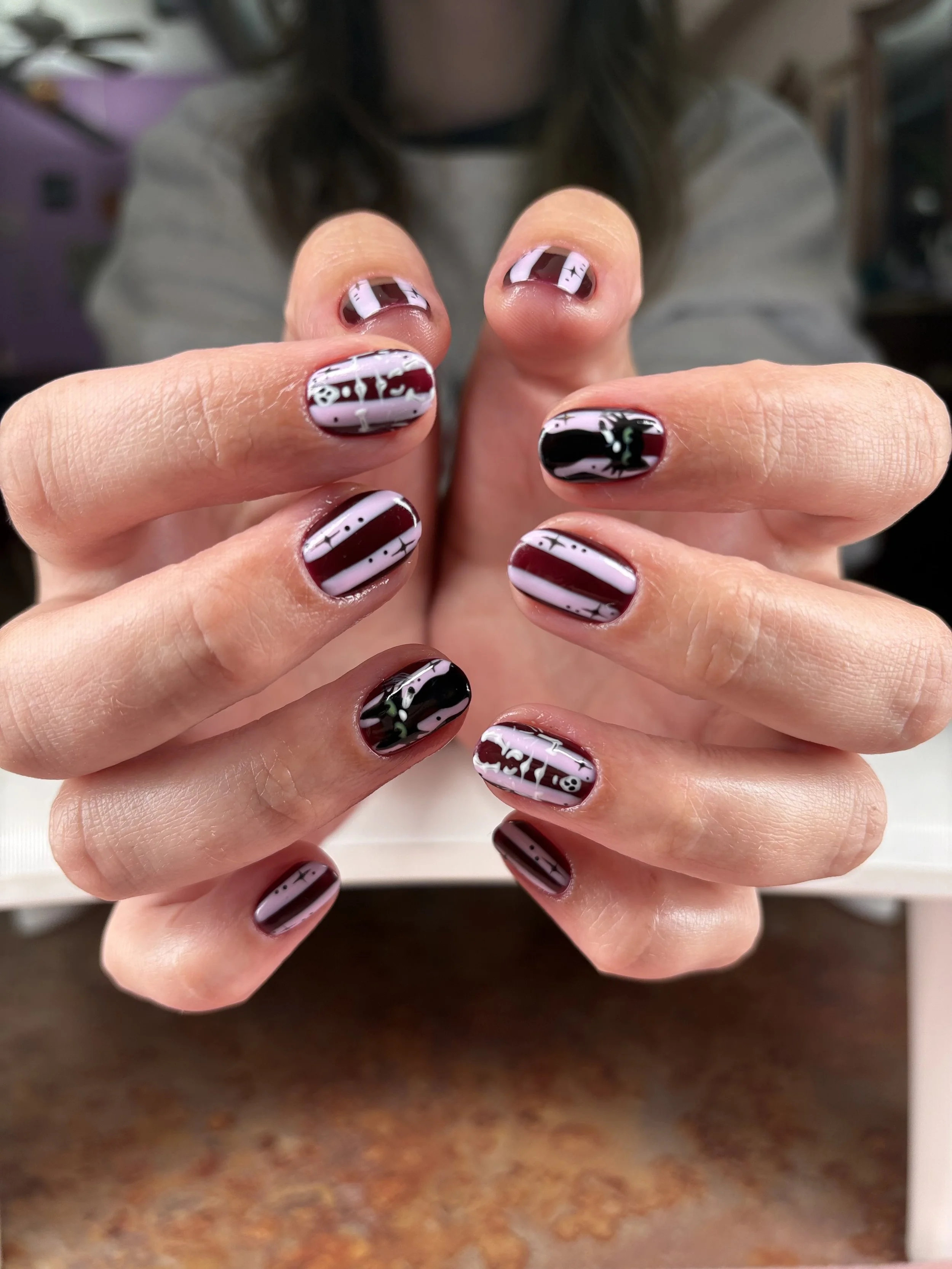 Custom burgundy, black, and lavender nail art with graphic stripes and fine white details at The Lon Next Door Salon & Spa in Grosse Pointe