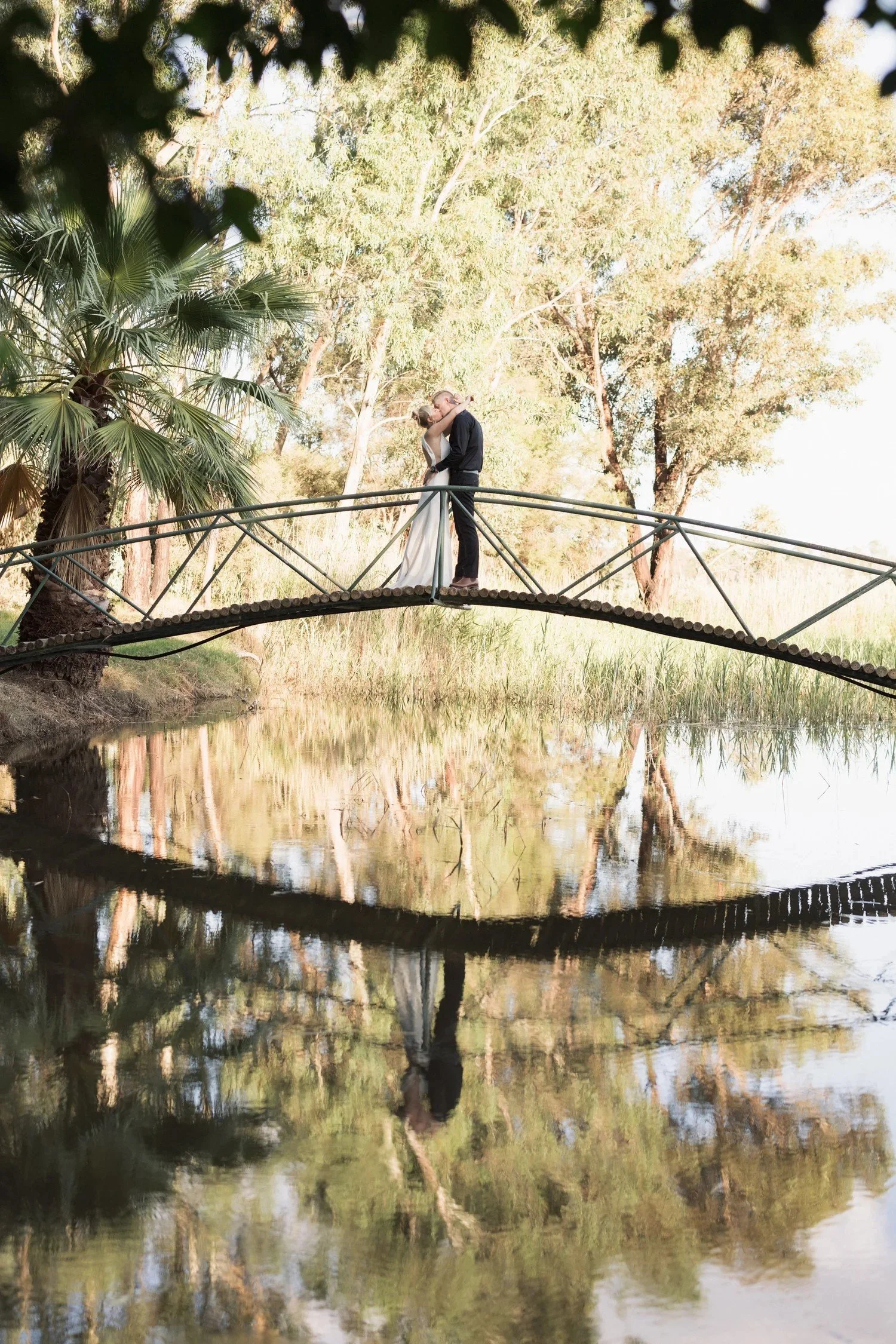 Newlyweds sharing a romantic moment on the bridge over the private lake at Greenfield Acres Wedding Venue, Riverland SA
