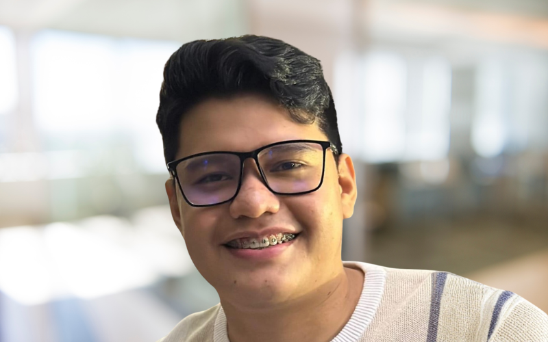 Young man wearing glasses and braces smiling indoors with a bright background