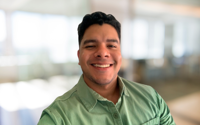 Smiling man in green shirt standing indoors with blurred background