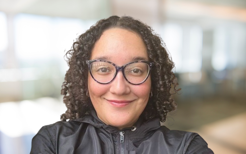 A woman with curly hair and glasses taking a selfie indoors.