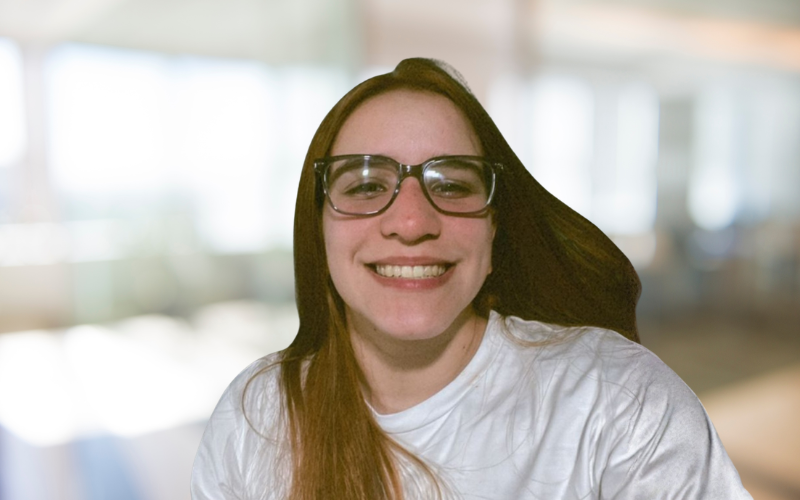 A young woman with long brown hair and glasses smiling at the camera.