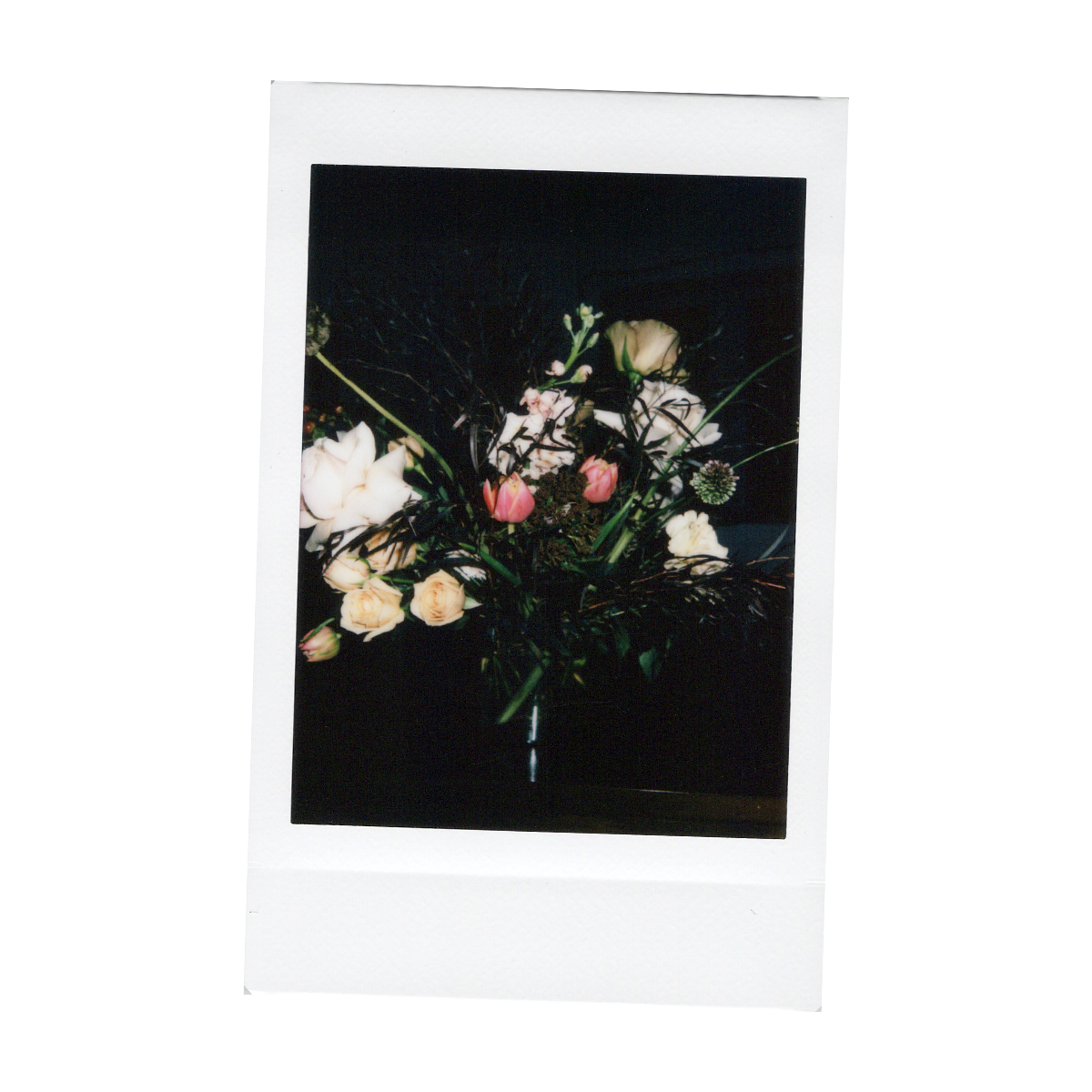 A printed photograph of a bouquet of flowers featuring white roses, pink tulips, and other assorted blossoms and foliage.