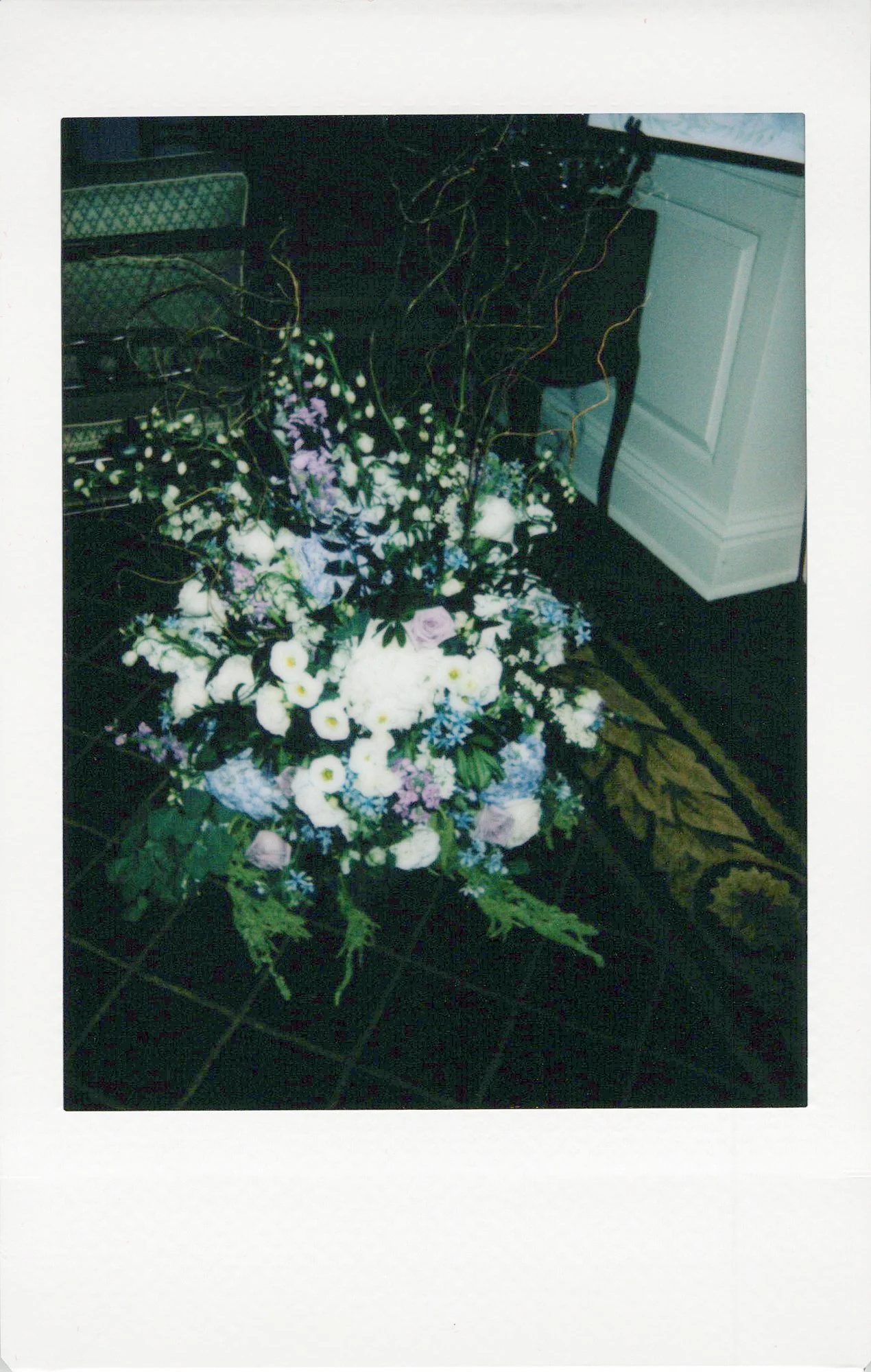 A large floral arrangement with white, purple, and pink flowers on a dark tiled floor, near a white cabinet and green upholstered furniture. Brand activation polaroids chicago.