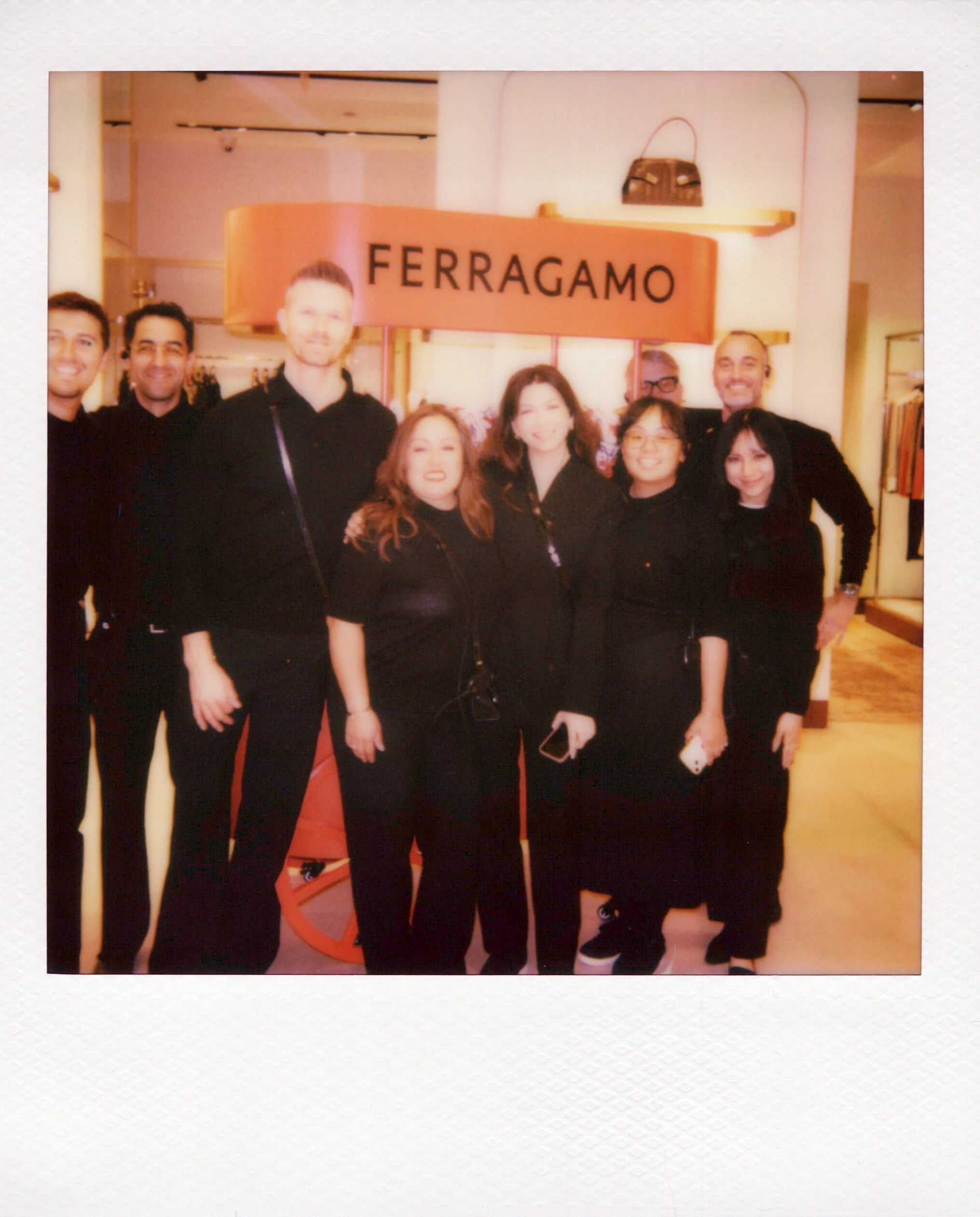 A polaroid of guests posing in front of a red sign that says "Ferragamo" and a brand event in Chicago.