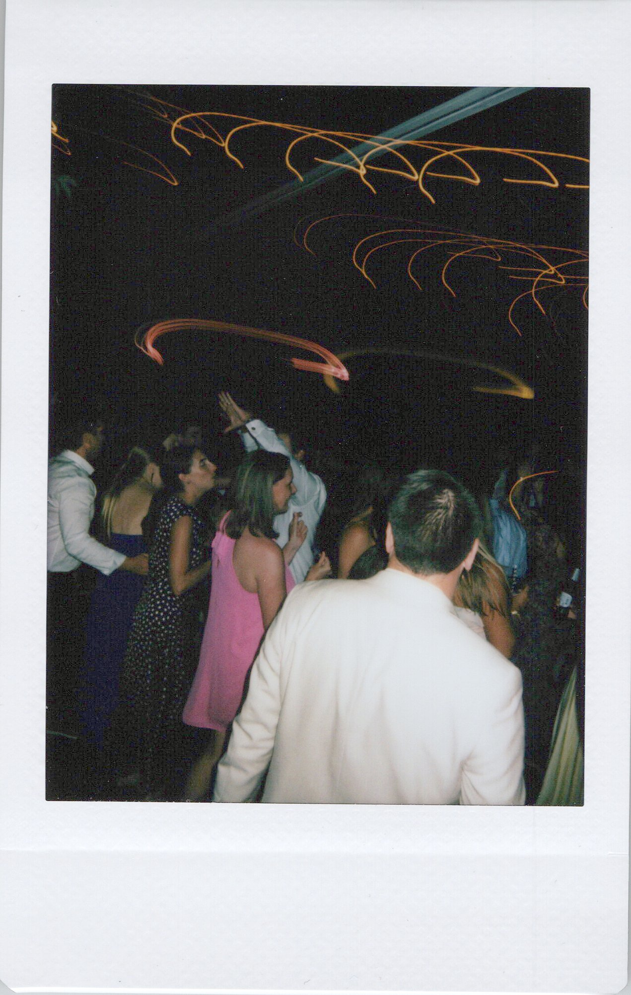 People gathered in a dark indoor setting with swirling light trails overhead, possibly at a party or event.