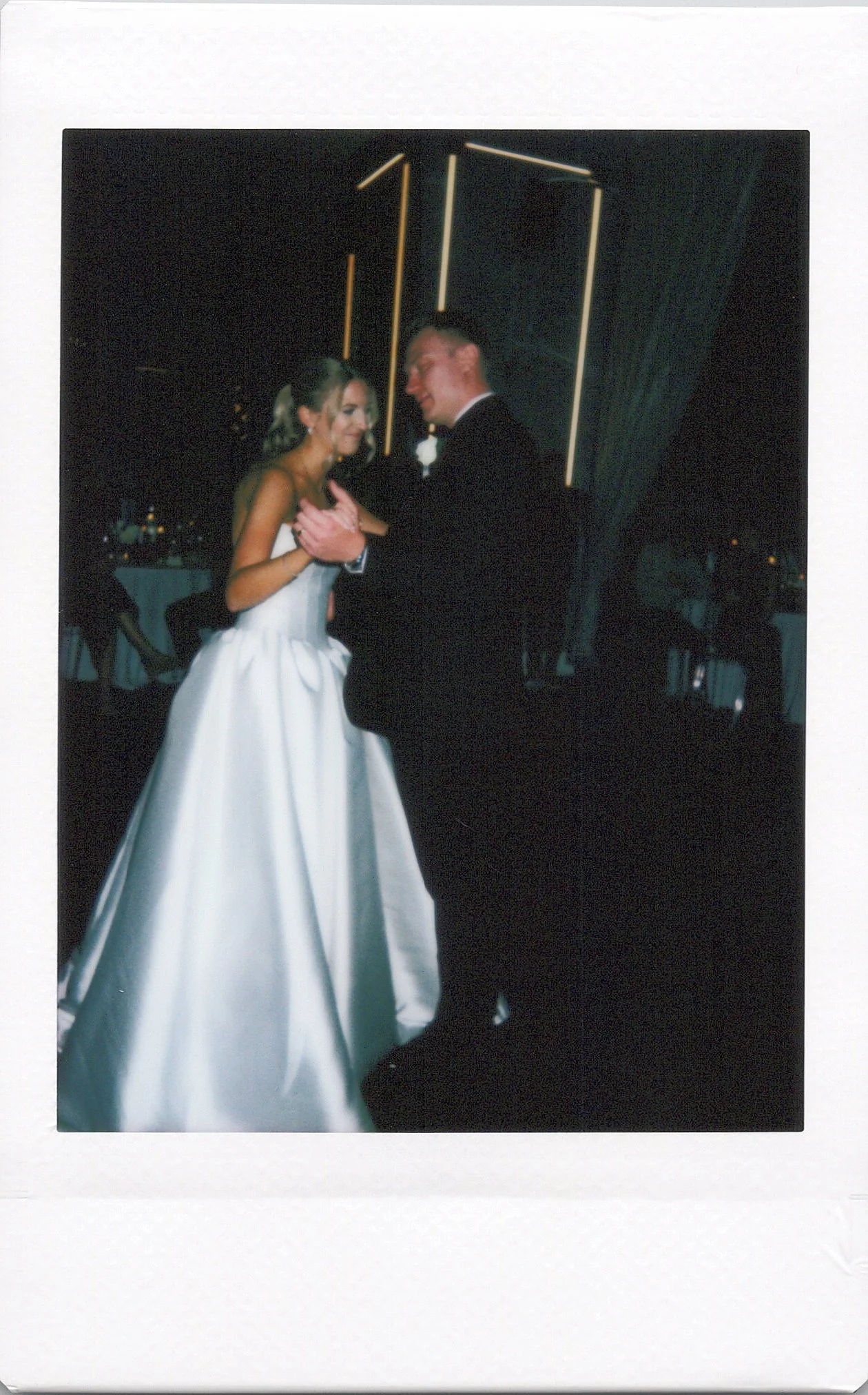 A polaroid photo of a Chicago bride and groom sharing a dance at their wedding reception, with the groom dressed in a tuxedo and the bride in a white wedding gown