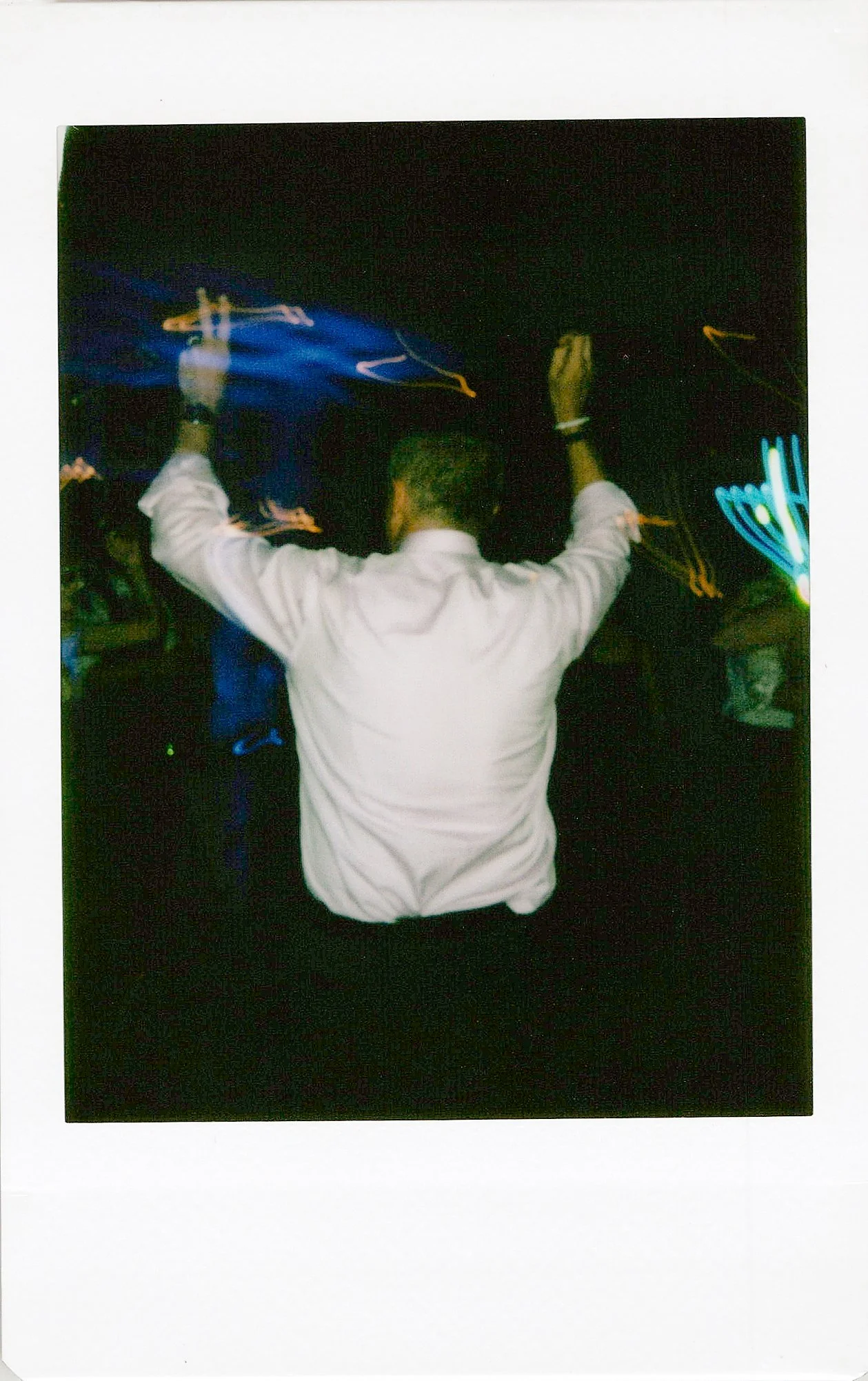 A person in a white shirt is standing with arms raised, surrounded by bright, colorful light streaks at night.