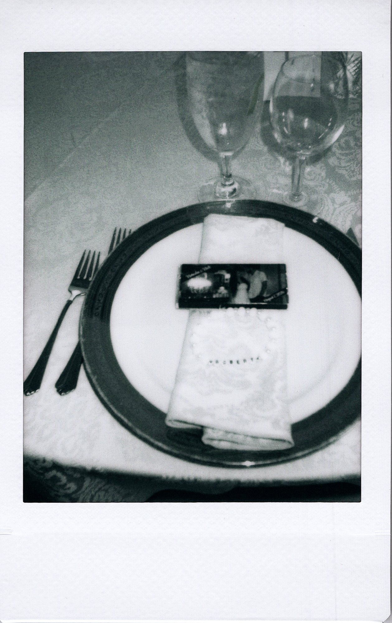 A table setting with two wine glasses, two forks, a plate with a napkin and a small chocolate bar, all arranged on a placemat.