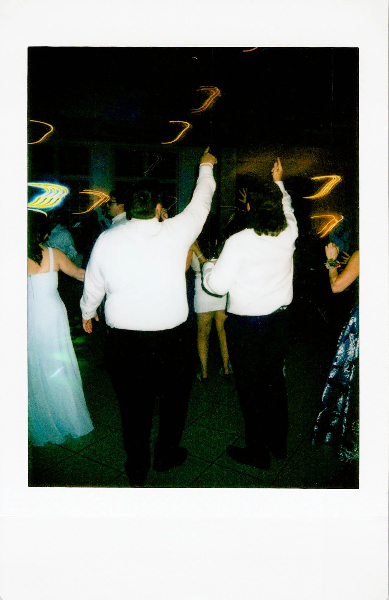 People dancing at a party or celebration with colorful lights and dark background.