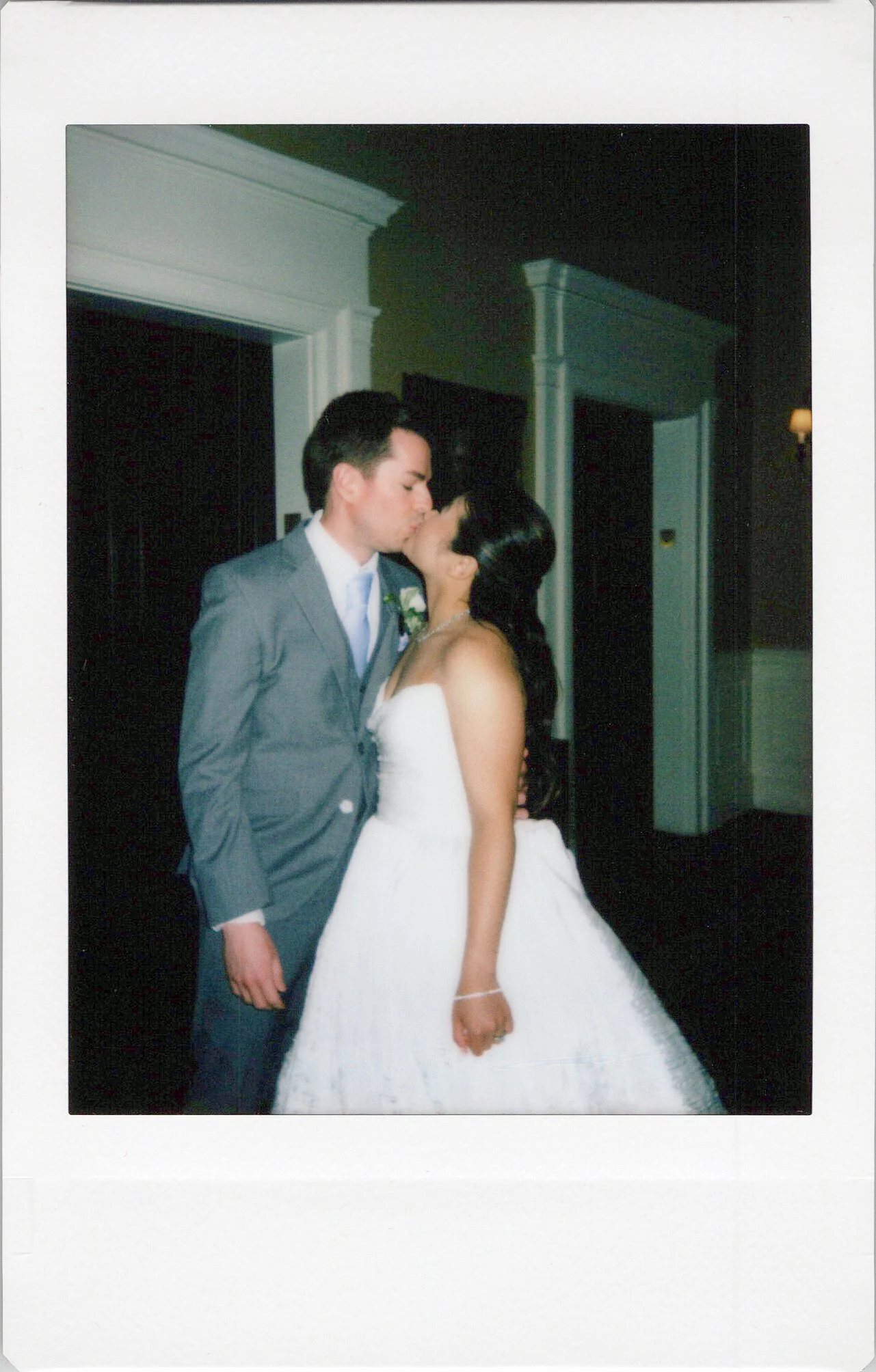 A polaroid photo of bride and groom sharing a kiss at their wedding reception cocktail hour.