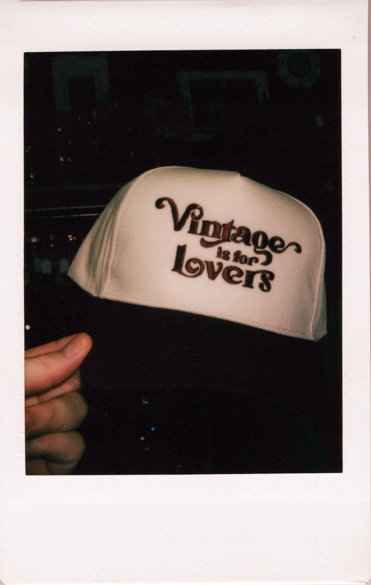 A white cap with embroidered text that reads 'Virgiles is for Lovers,' being held by a person's hand.