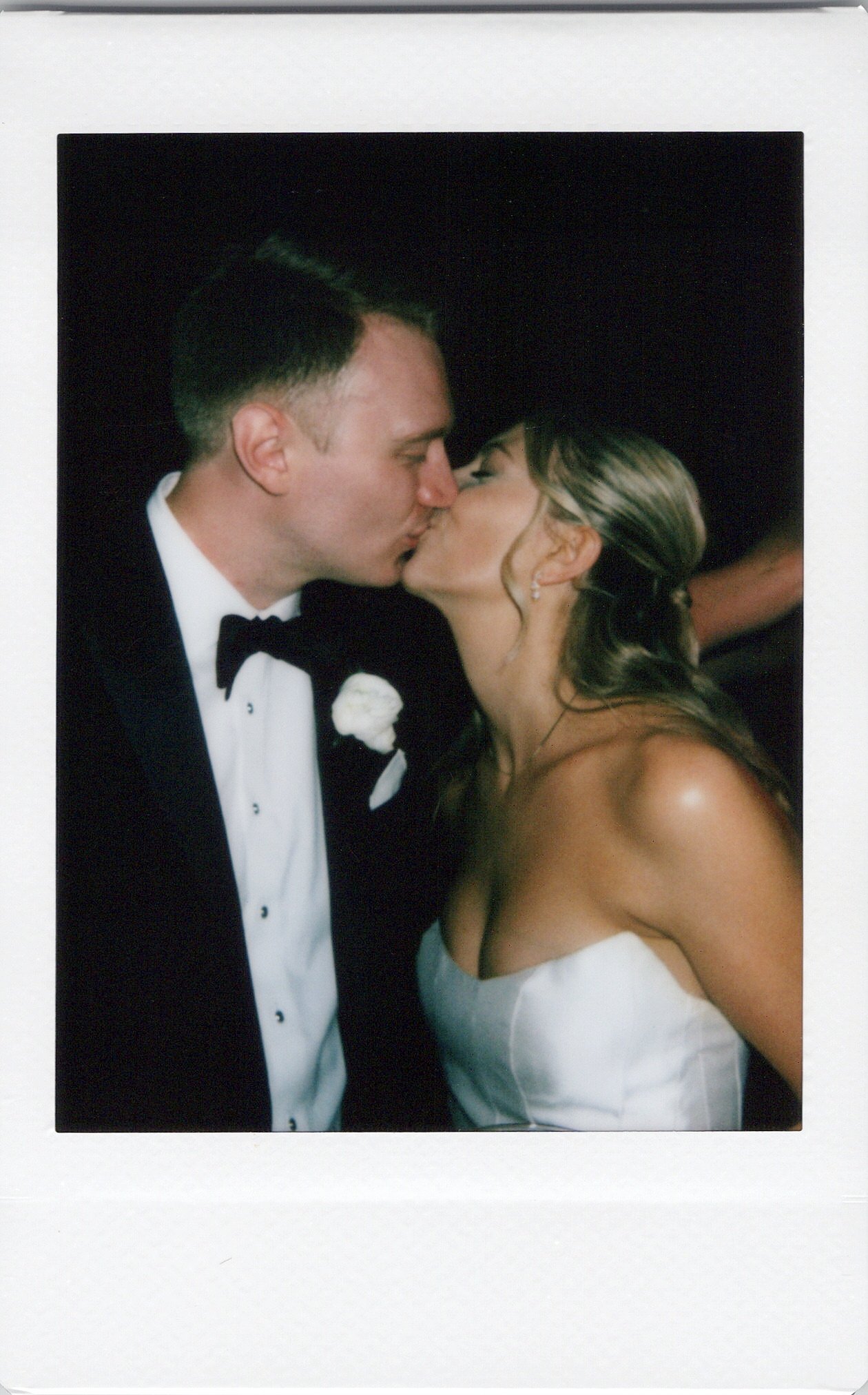 A polaroid photo of a newlywed couple in formal wedding attire sharing a kiss.
