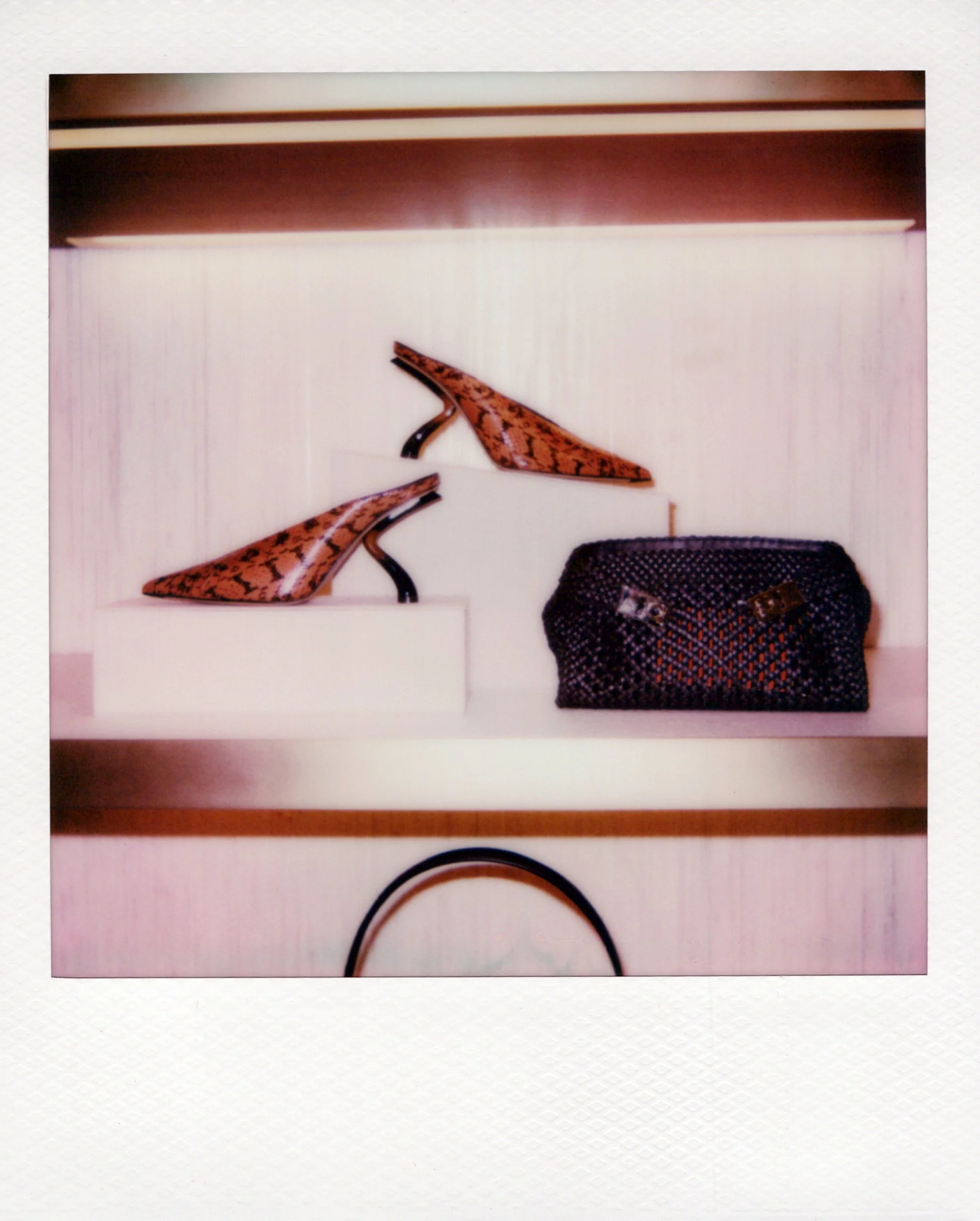 Polaroid picture of two orange and black snakeskin-patterned high heels and a black textured handbag on a white surface at a Chicago brand activation.
