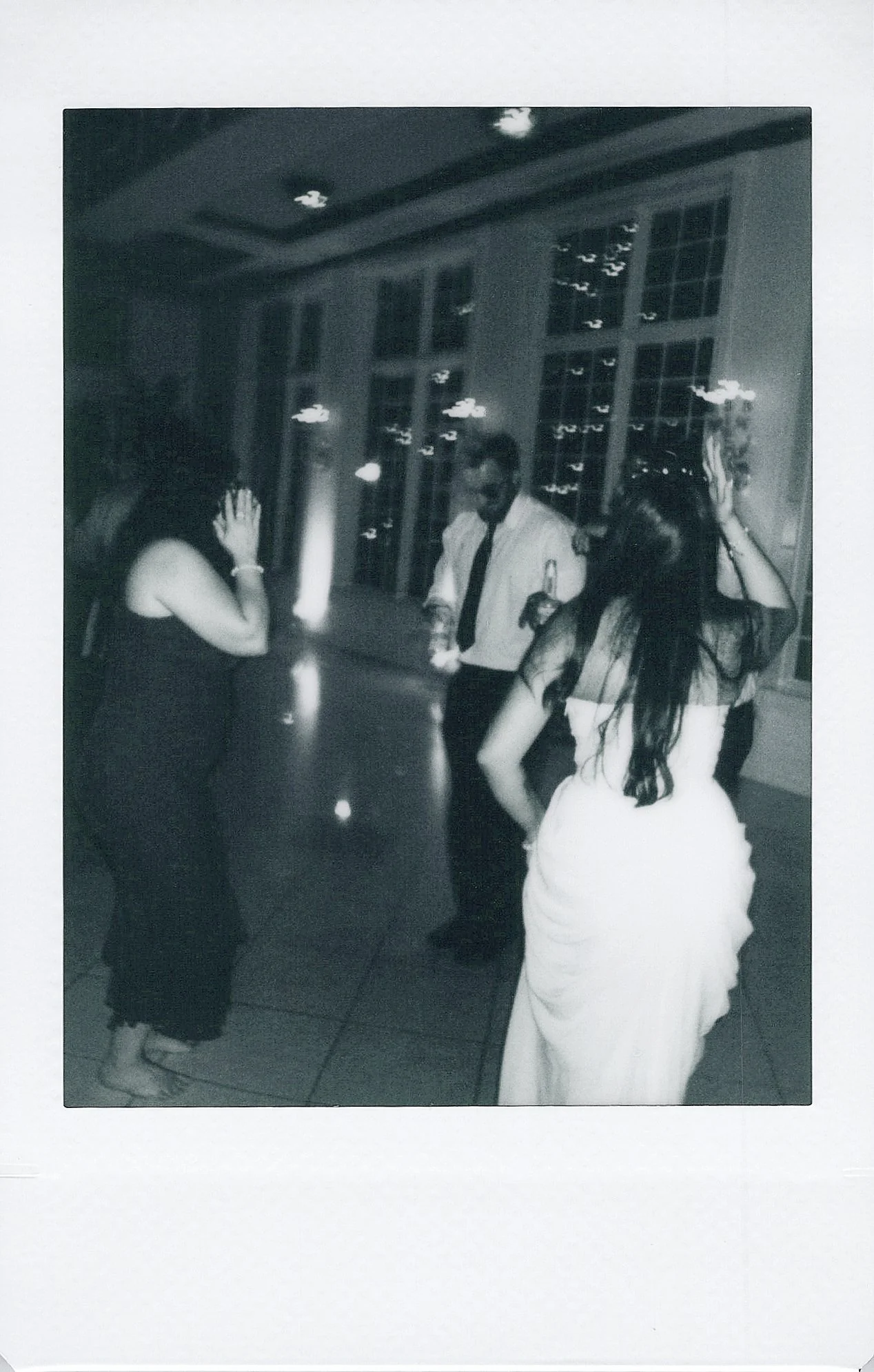 Black and white photo of people dancing at a party or social gathering, with a large window in the background.