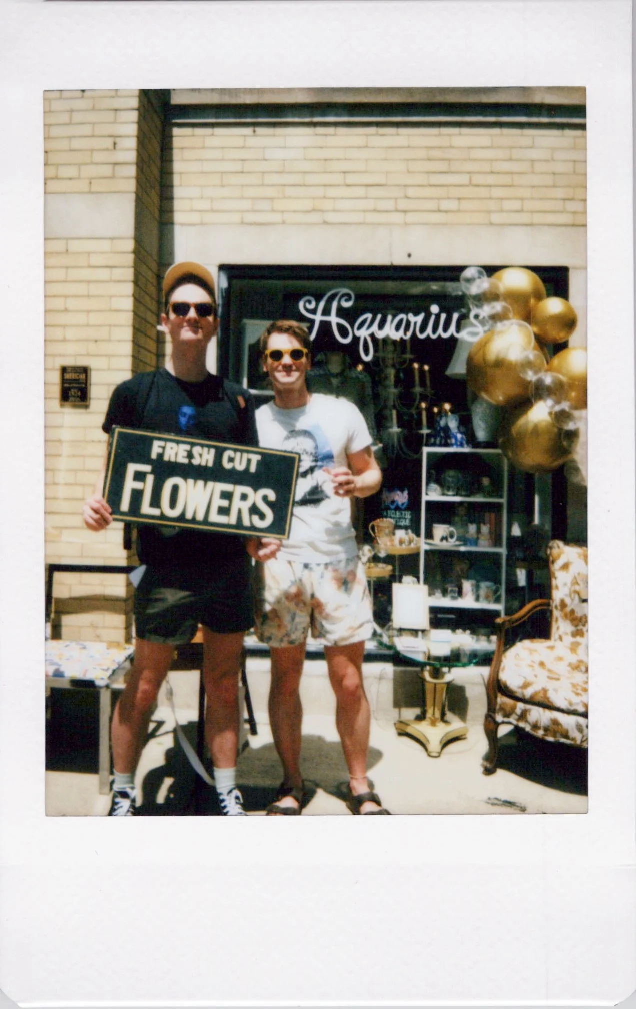 instant photo of a gay couple holding a sign that says "fresh cut flowers" at a vintage store day pop-up in chicgao