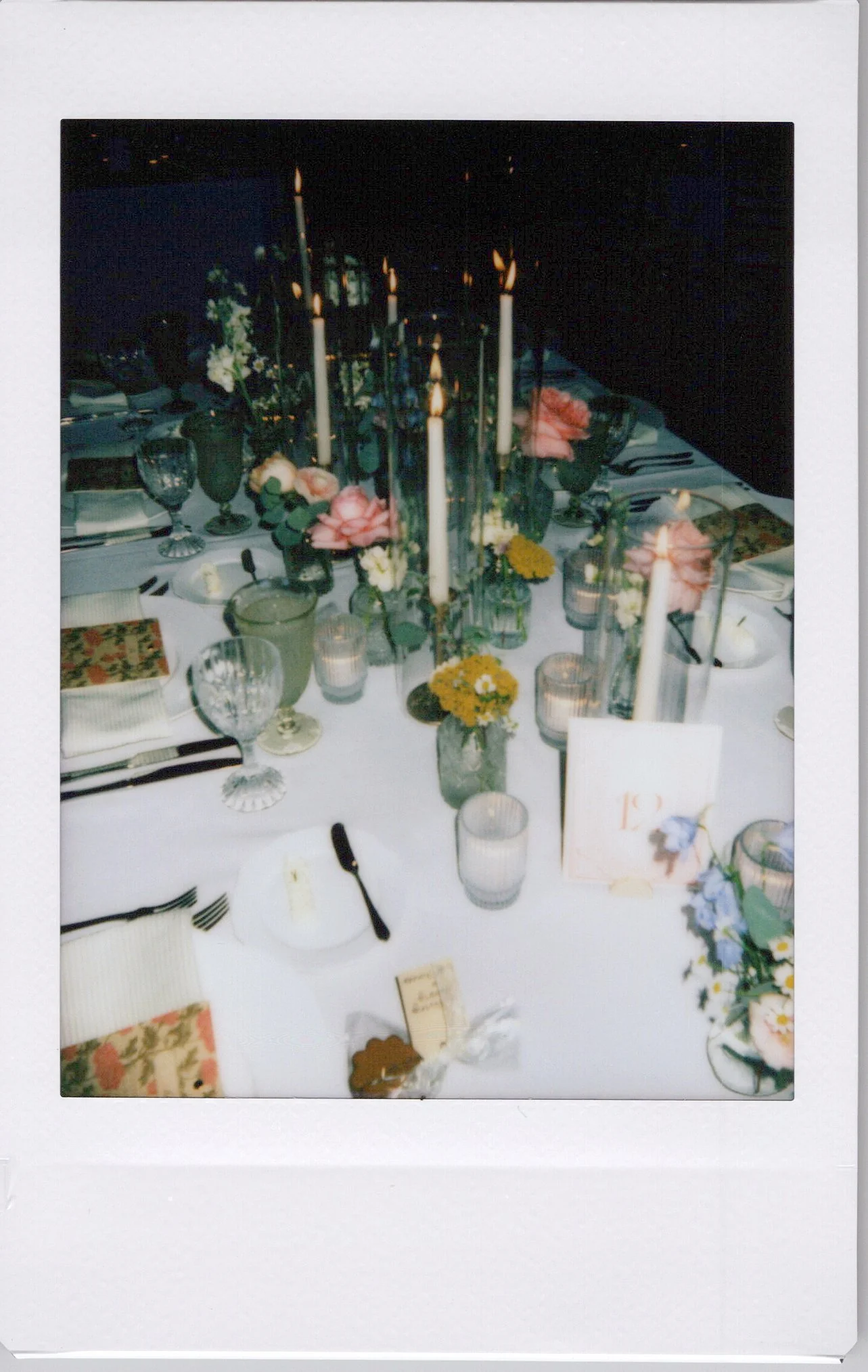 A table set for a formal event with white tablecloth, glassware, candles, flowers, and place settings, in a dimly lit room.