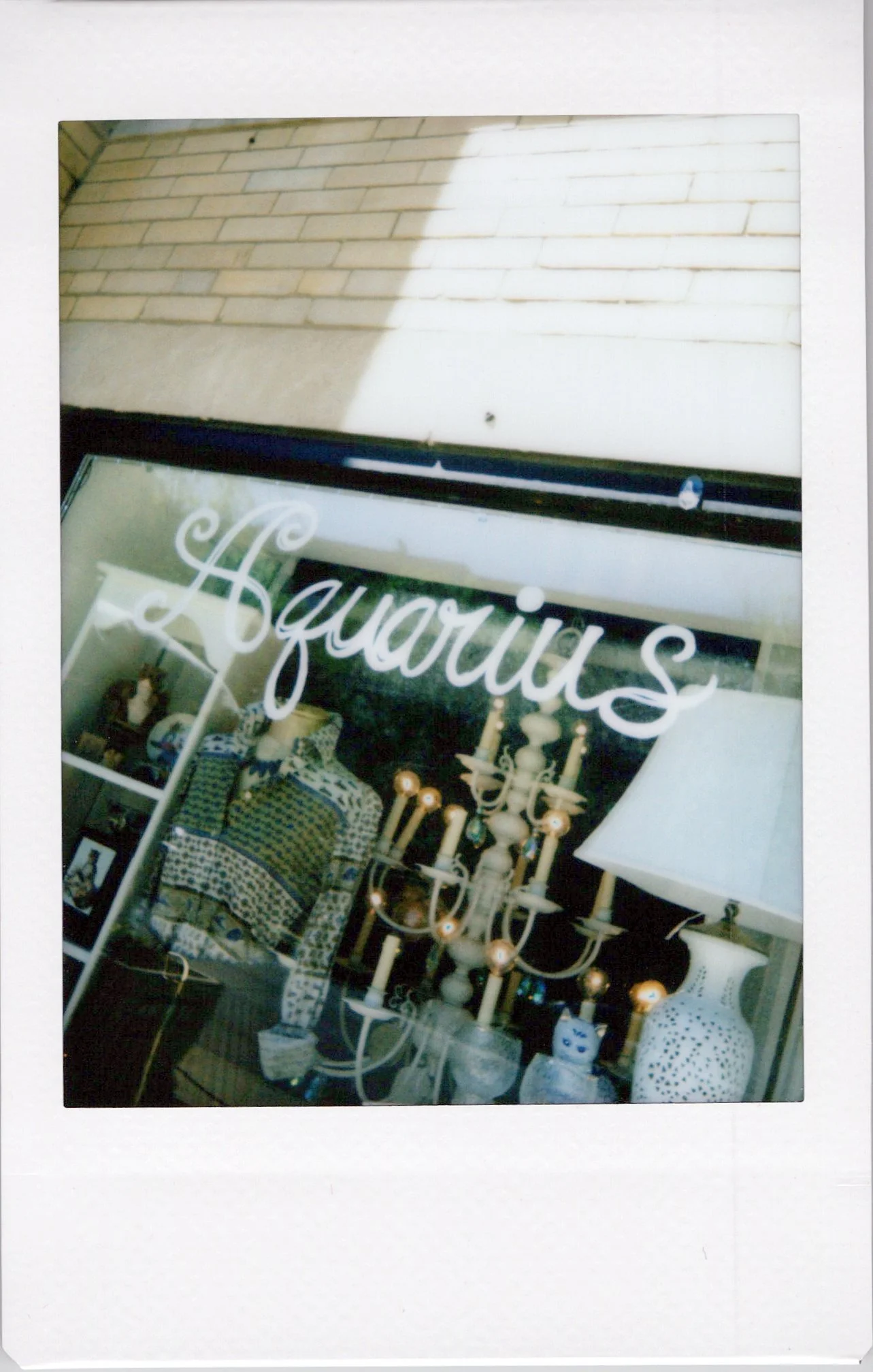 A display window with the word "Lauri" written in cursive, showing home decor items such as a bed with patterned bedding, a large white lamp, a ornate chandelier, and decorative vases with blue patterns.
