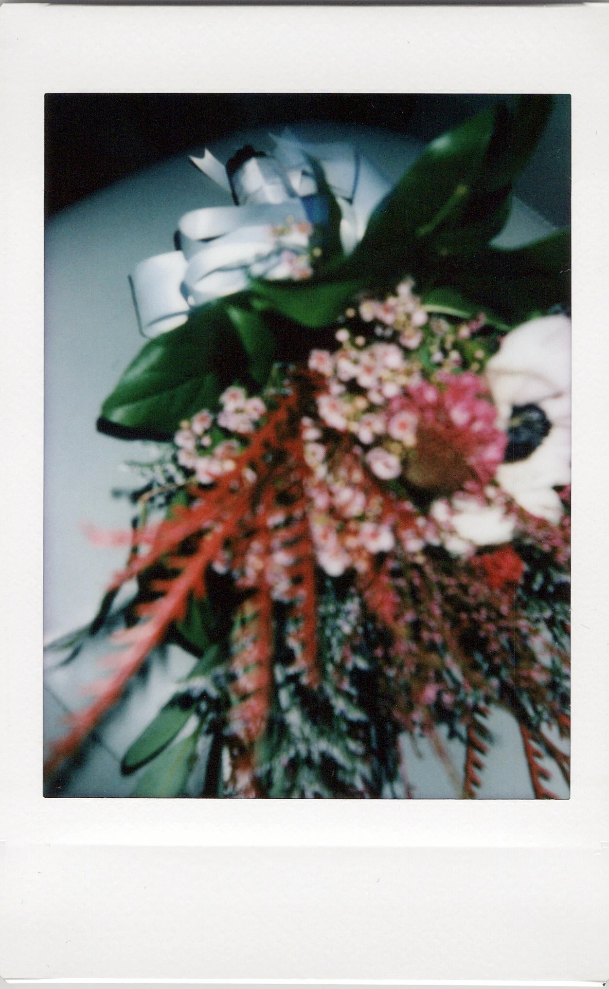Close-up of a floral boutonniere with white flowers, pink and red accents, and green leaves, on a white background.