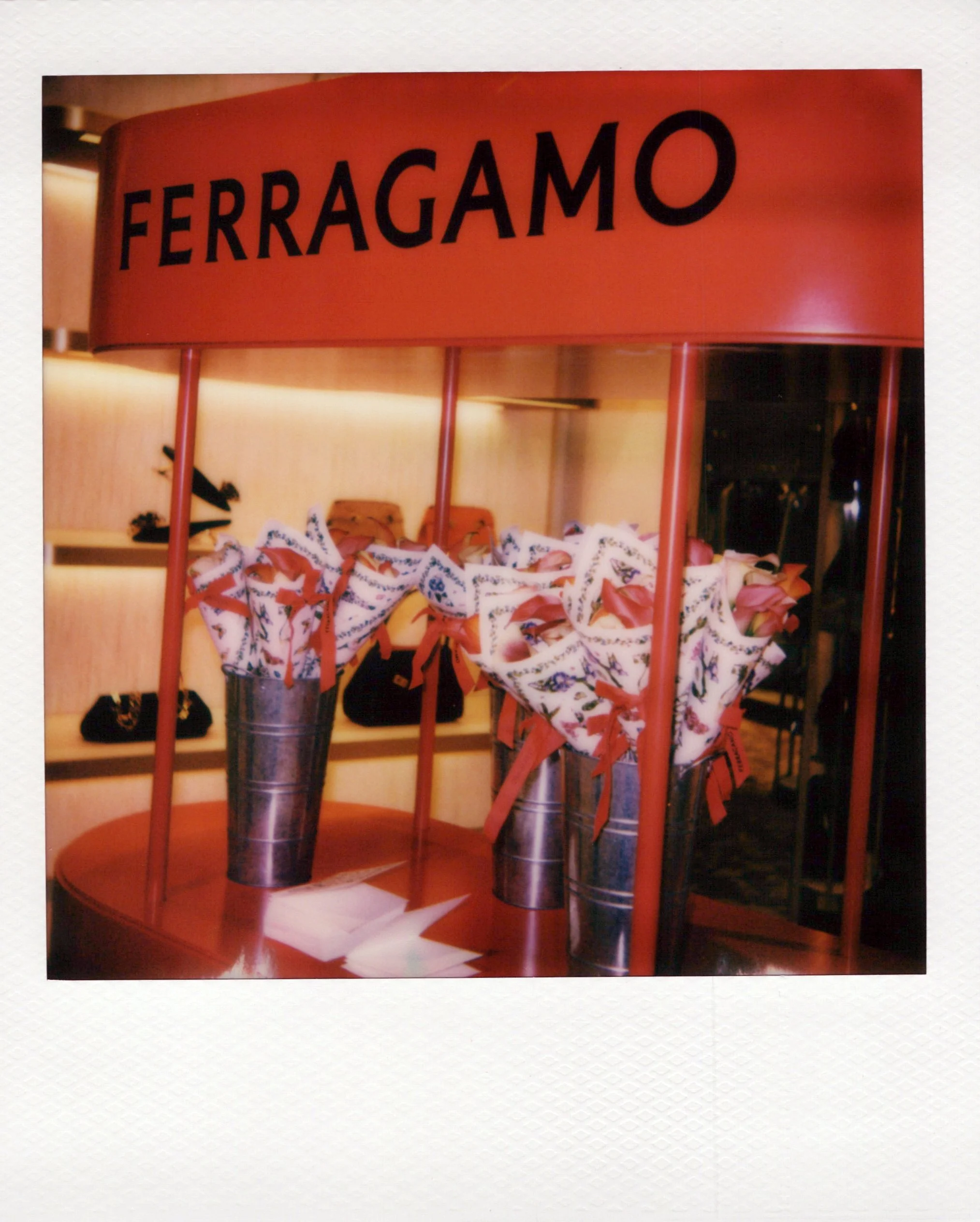 Display stand with the brand name 'FERRAGAMO' on a red sign, featuring wrapped gift boxes and some blending into the background for a polaroid mother's day brand activation with Instant Photo Chicago.