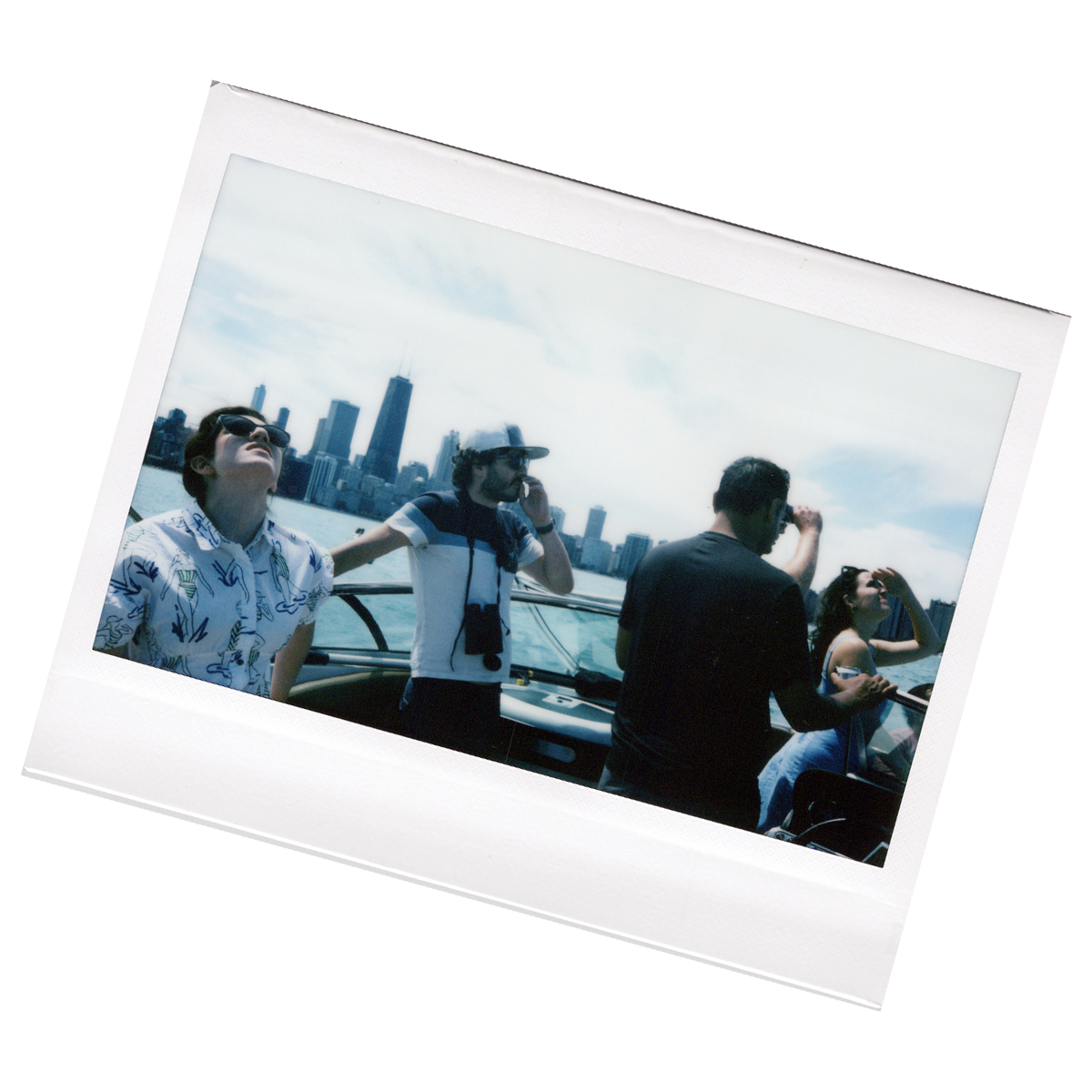 Group of young adults on a boat in front of the Chicago skyline, some are taking pictures and enjoying the view.