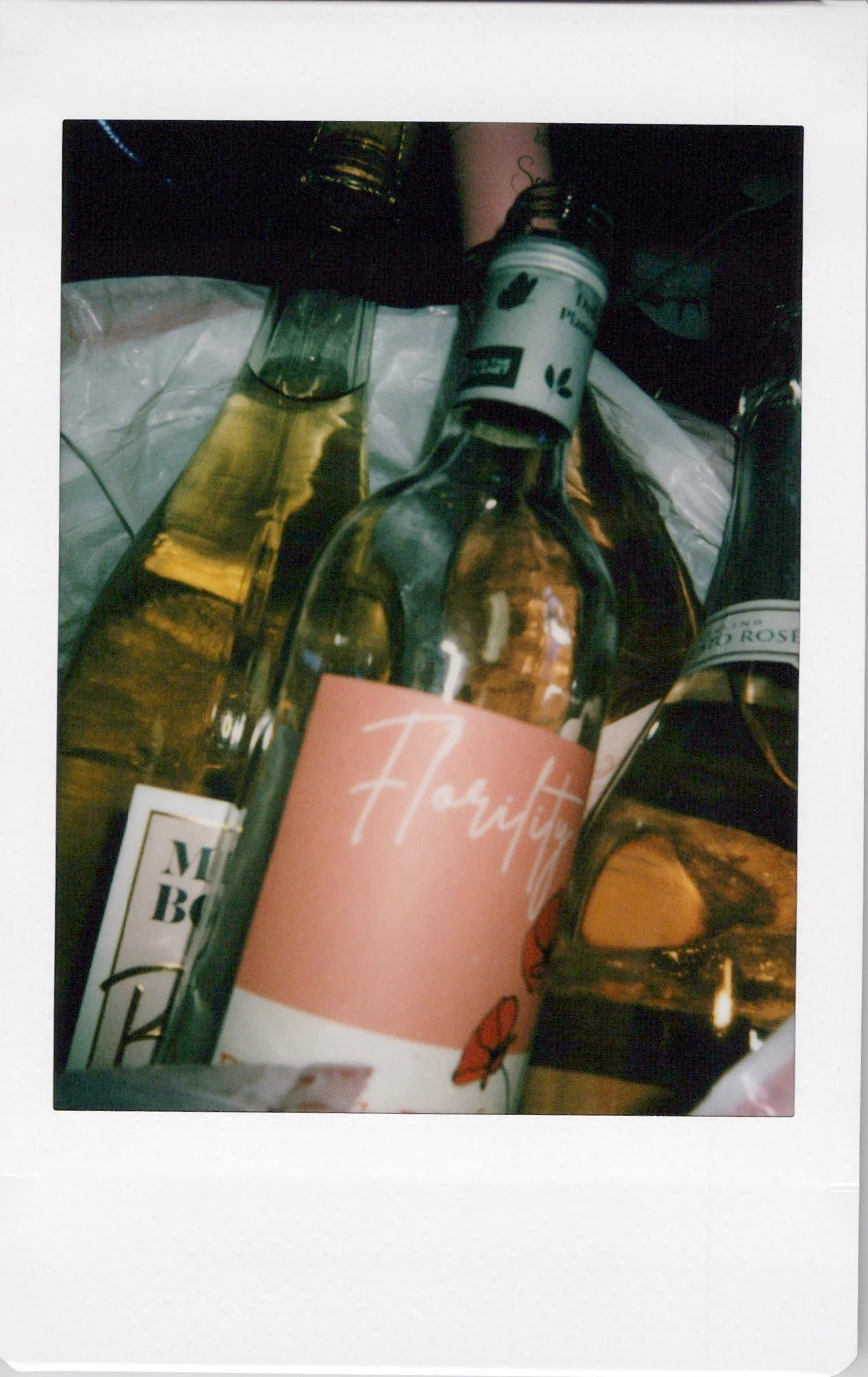 Close-up of various bottles, including a rose wine bottle with a pink label, and other beverage containers, arranged on a surface.