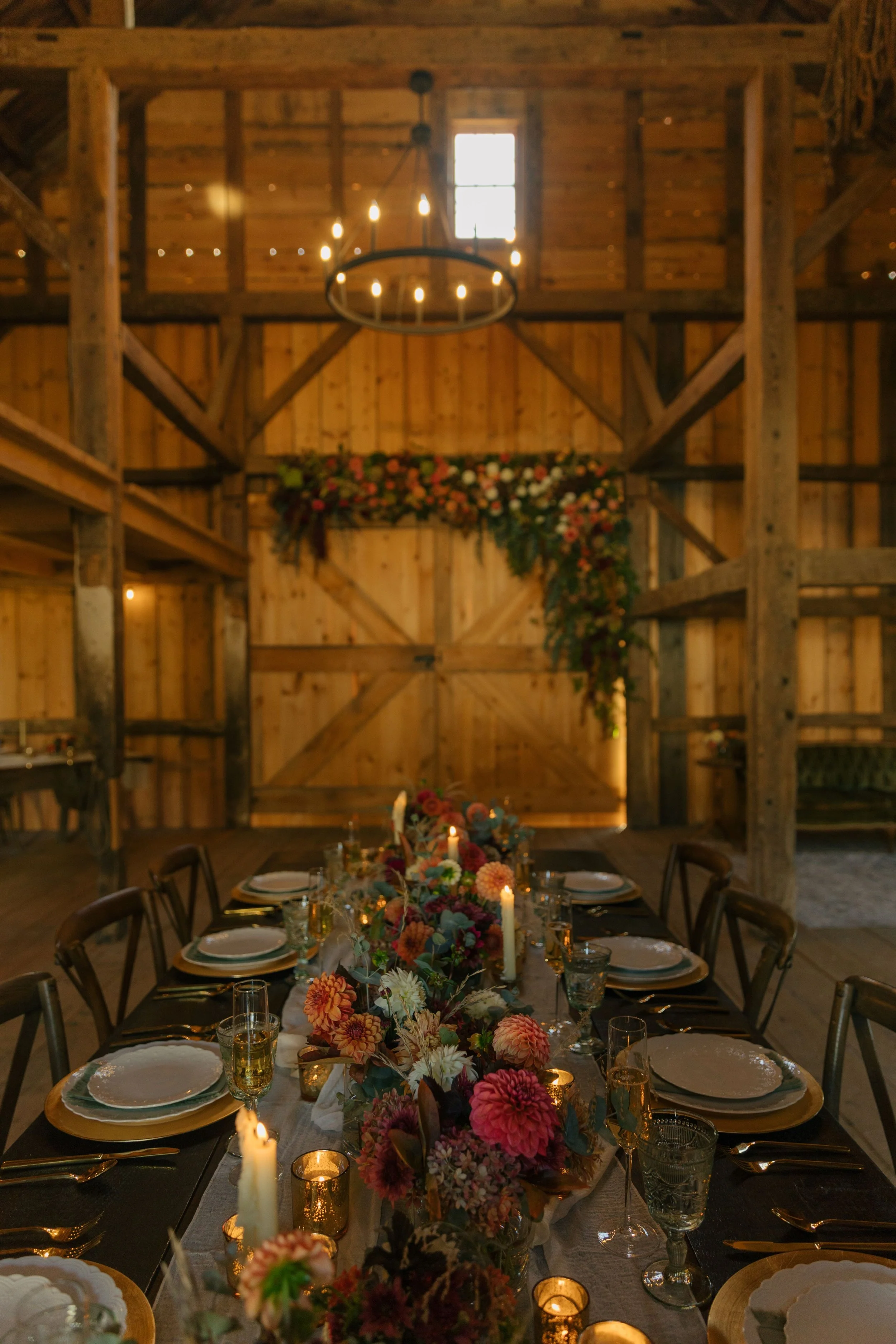 Rustic barn interior decorated for a wedding or celebration with a long table, floral centerpiece, candles, and dinnerware.