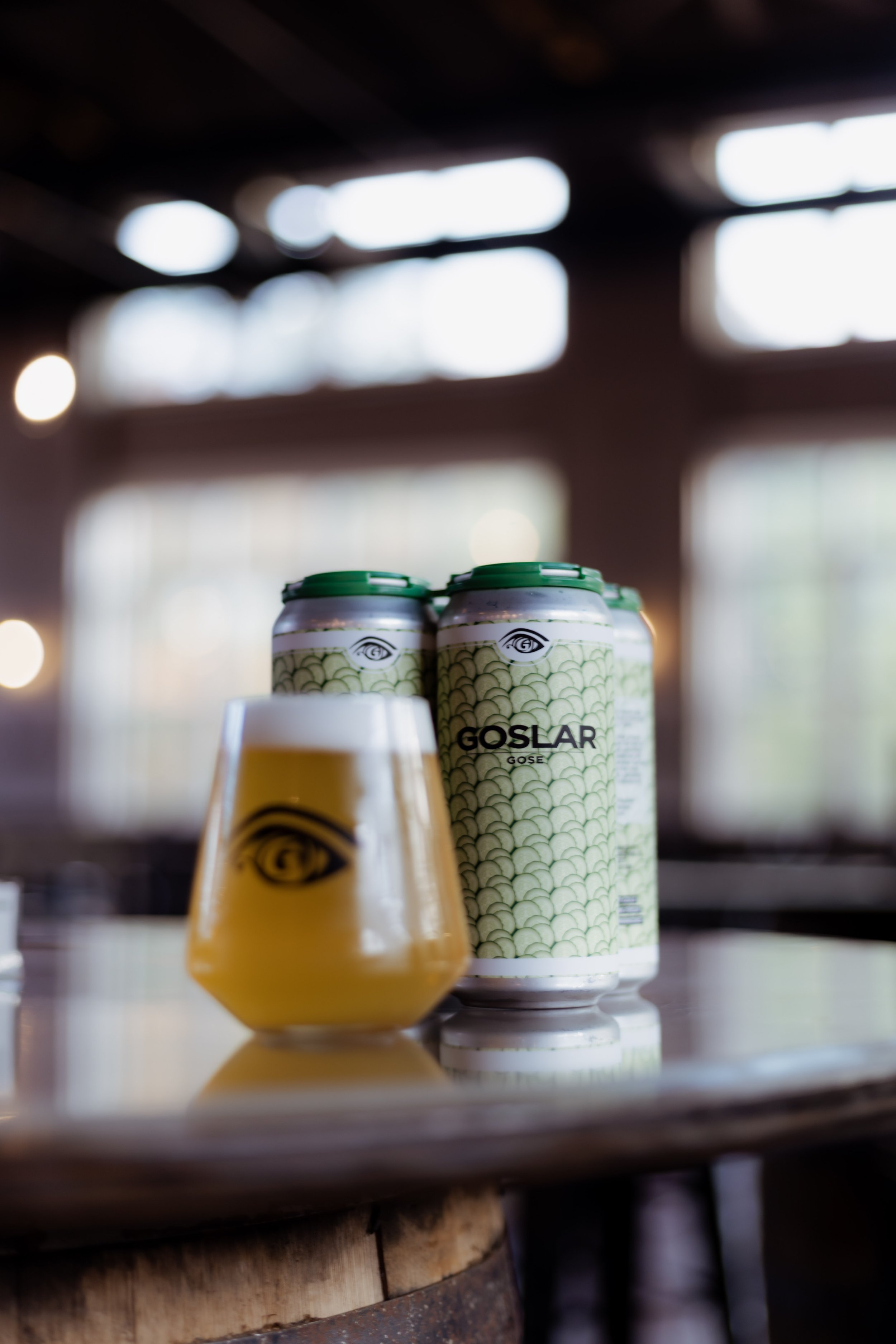 Cans of Goslar Gose beer with a glass poured from one of the cans, set on a wooden table.