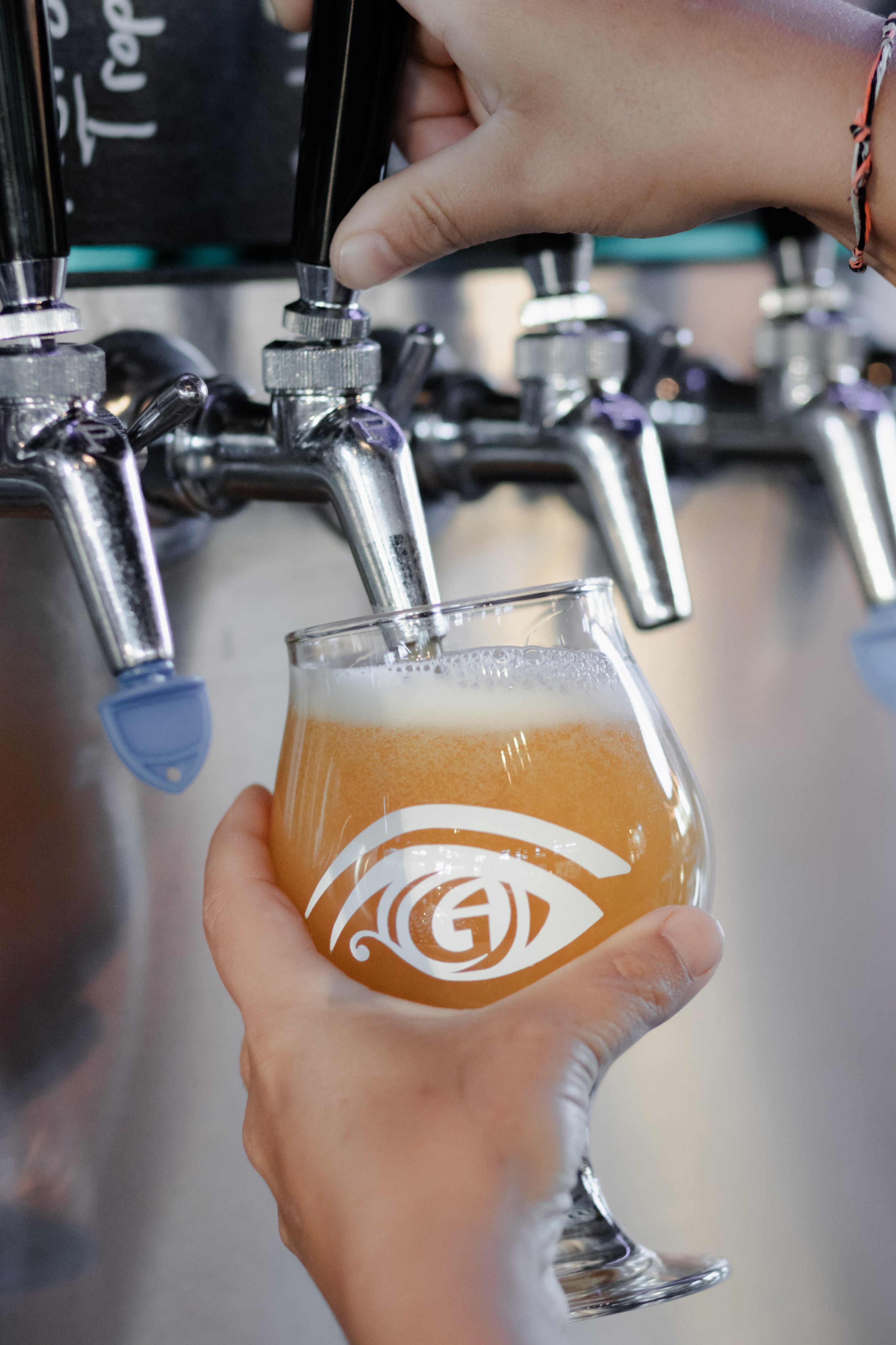 Person pouring beer from tap into a glass with logo, using their hand, in a brewery or pub setting.