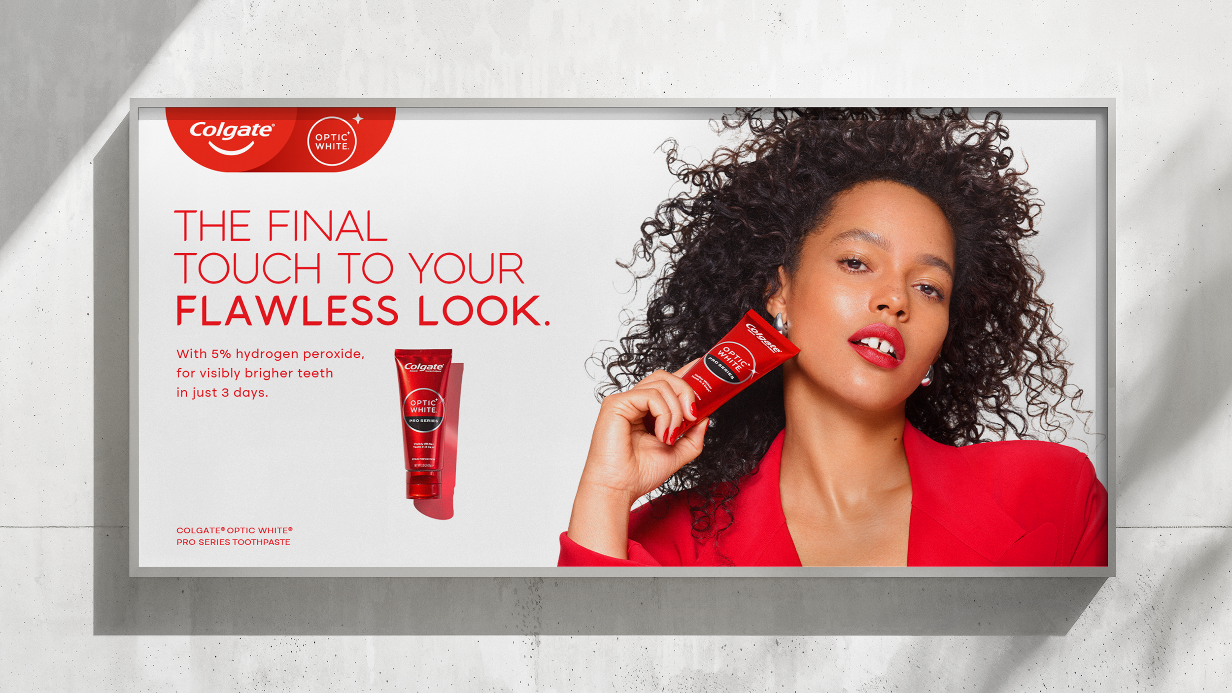 A woman with curly hair and red lipstick holding a tube of Colgate Optic White toothpaste. The billboard advertises teeth whitening with 5% hydrogen peroxide, promising brighter teeth in 3 days.