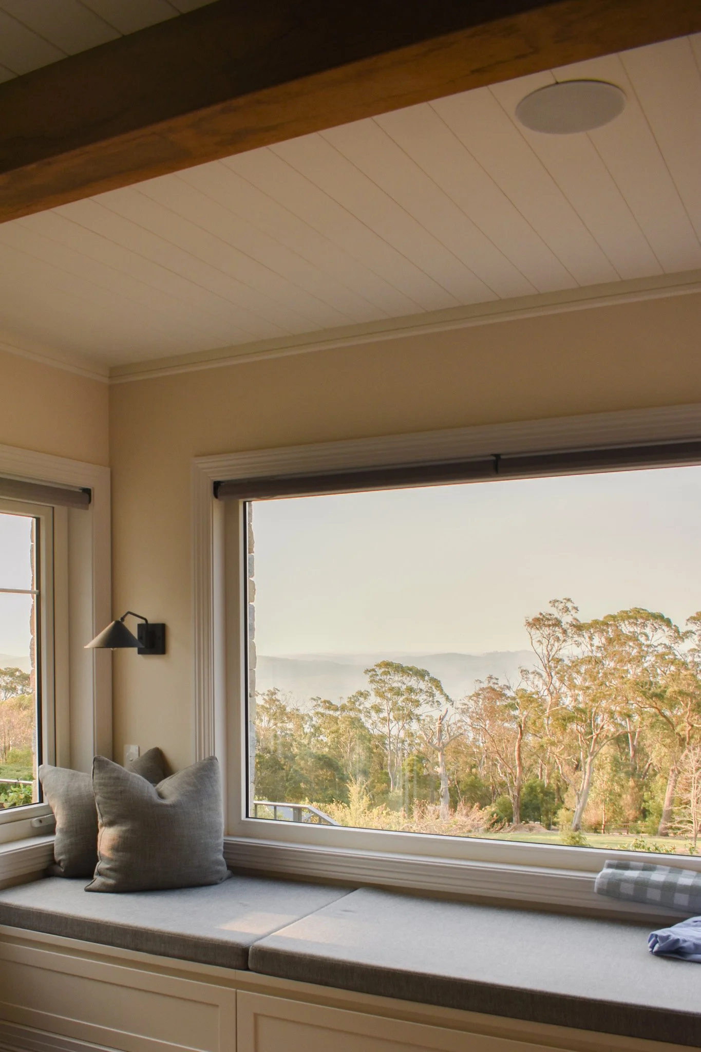 A cozy window seat with cushions and pillows, overlooking a scenic view of trees and distant hills.