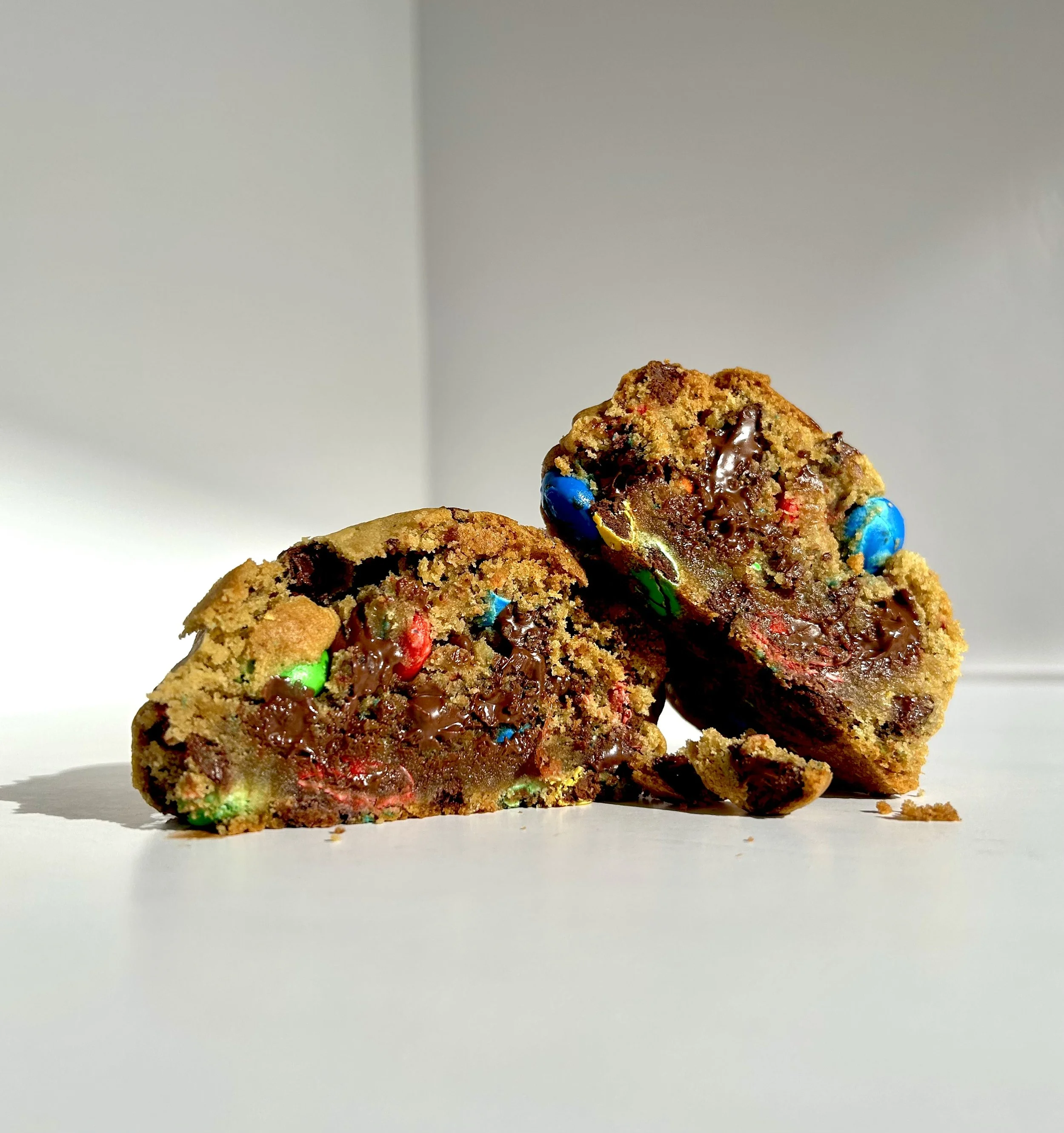 Two cookies with colorful candies and melted chocolate inside, broken in half.